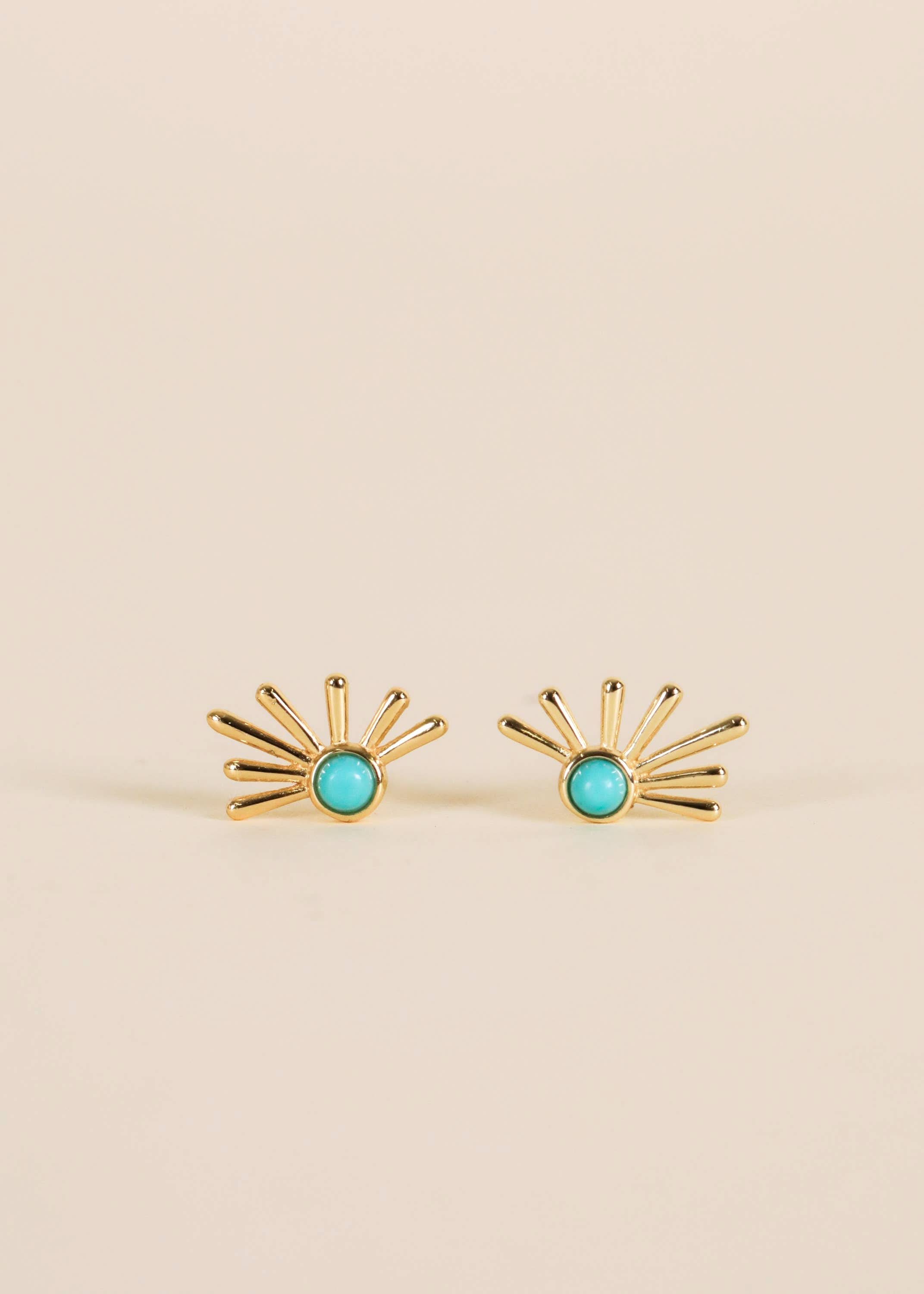 Gold earrings with turquoise stones on a beige background