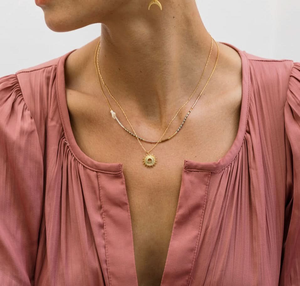 Person wearing a gold necklace with a pink top