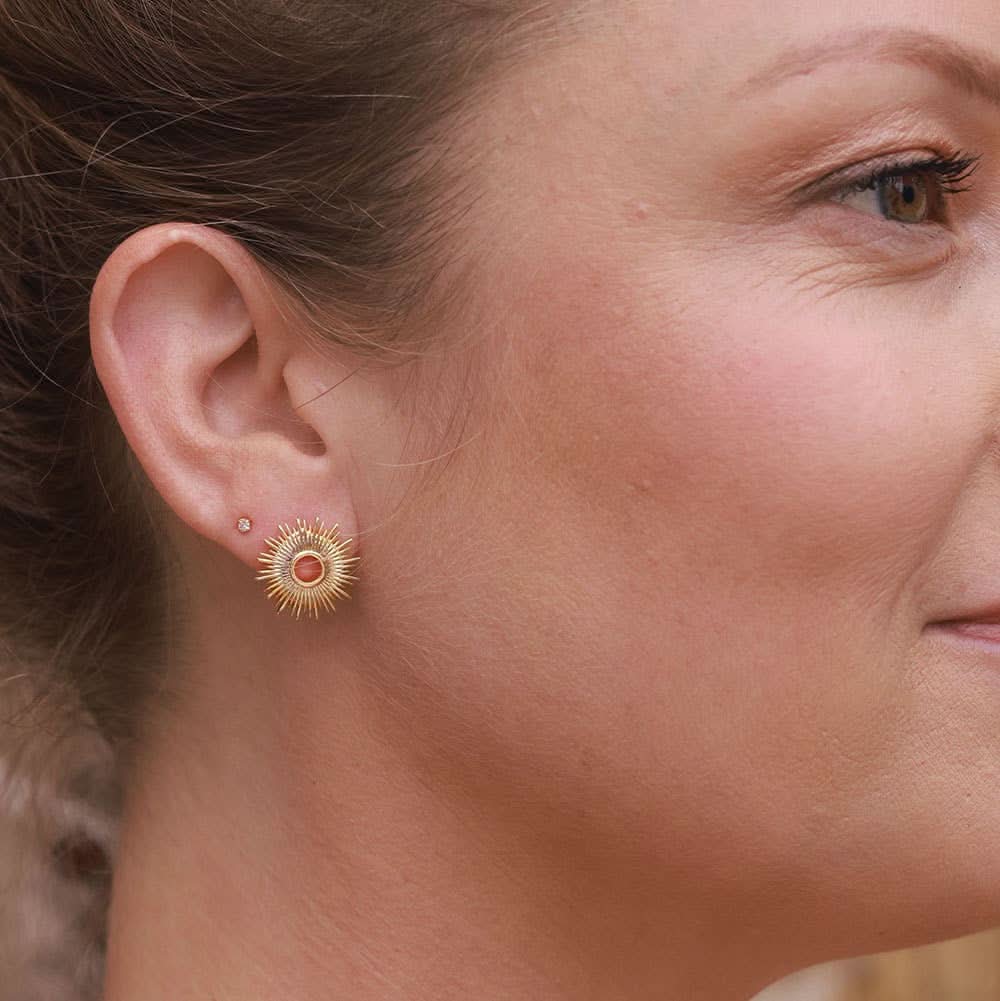 Woman wearing gold stud earrings in a circle sunburst pattern 