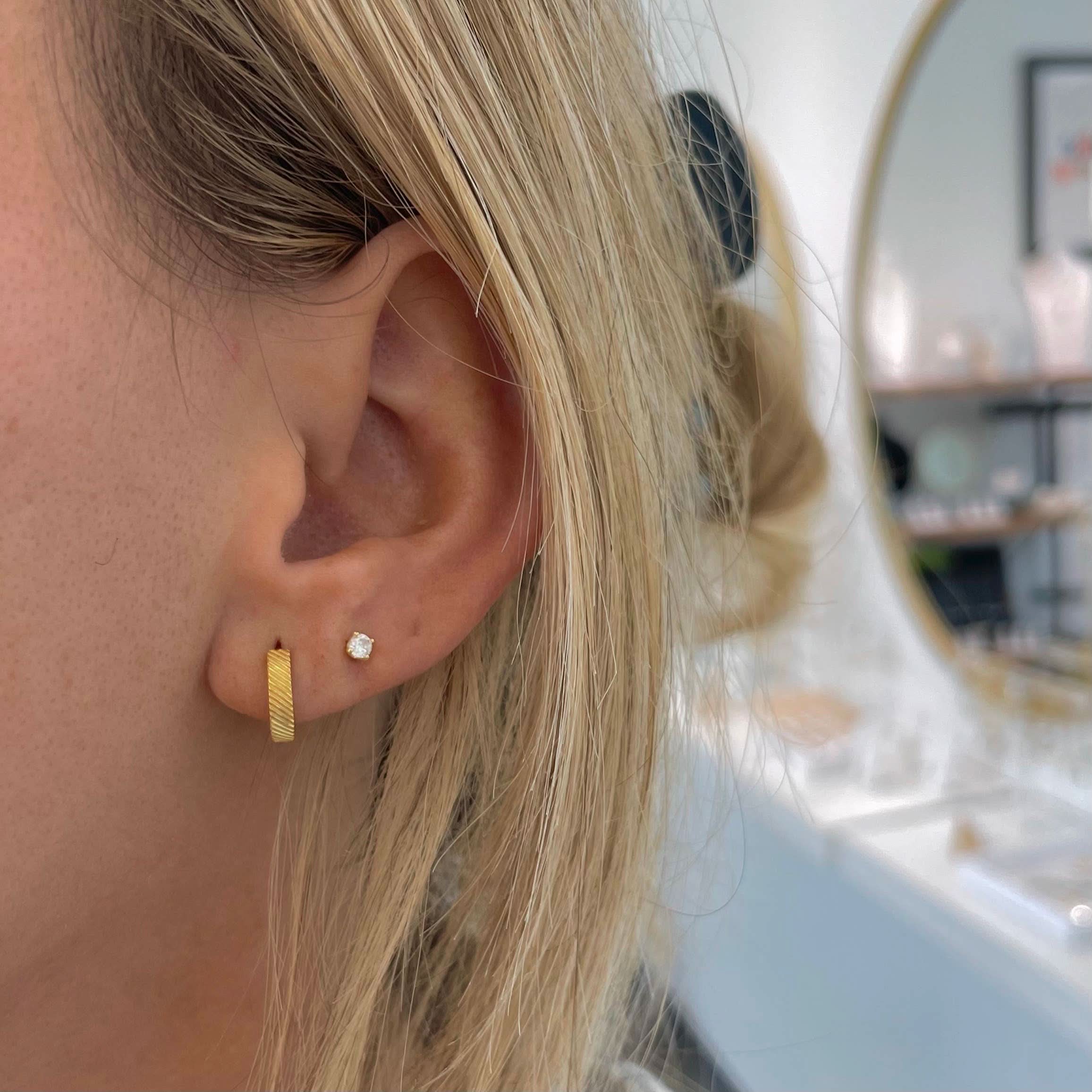 Woman wearing textured gold huggie loop hoop earrings and studs