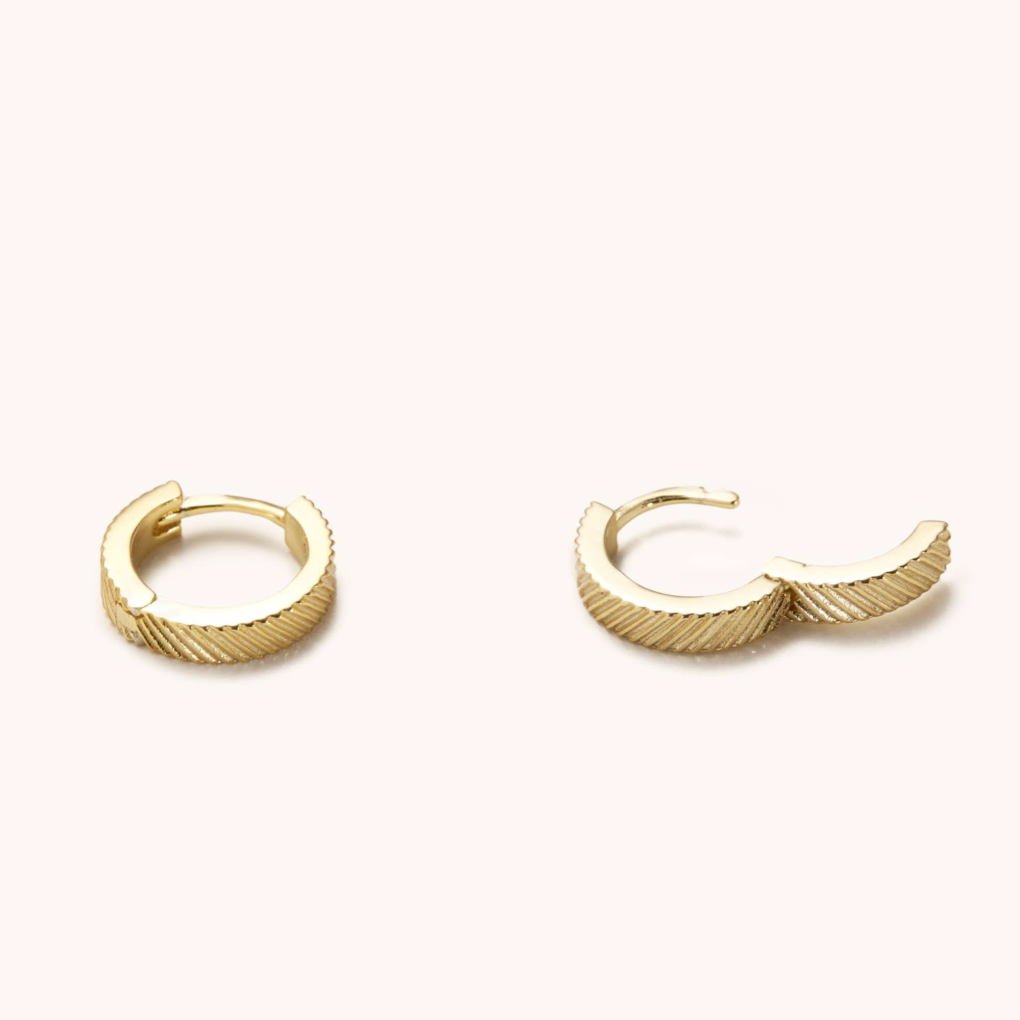 Pair of textured gold huggie loop hoop earrings laying on a white background 