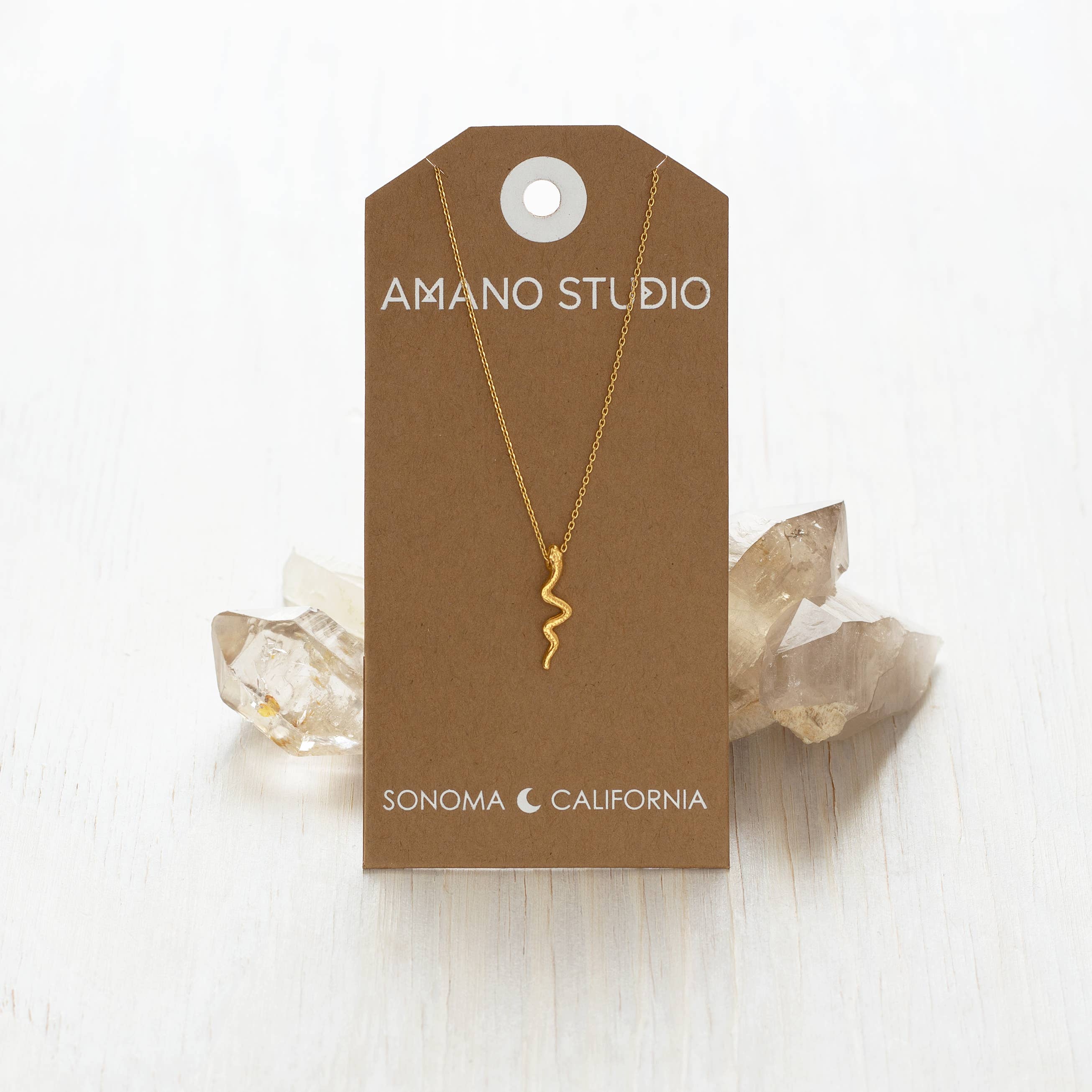 Gold necklace on a brown Amano Studio card with crystals in the background