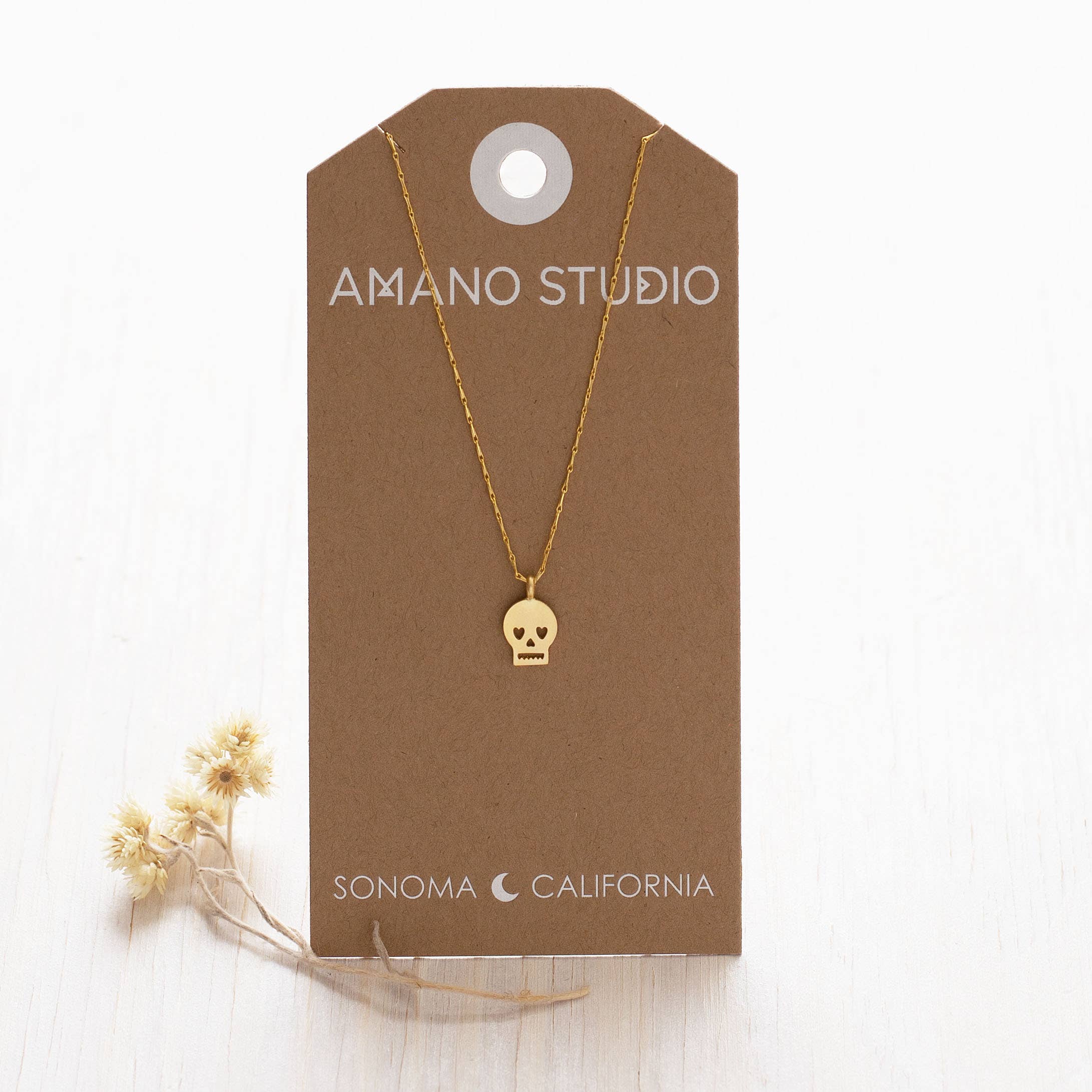 Gold necklace with skull pendant on a brown AMANO STUDIO card with 'Sonoma, California' text.