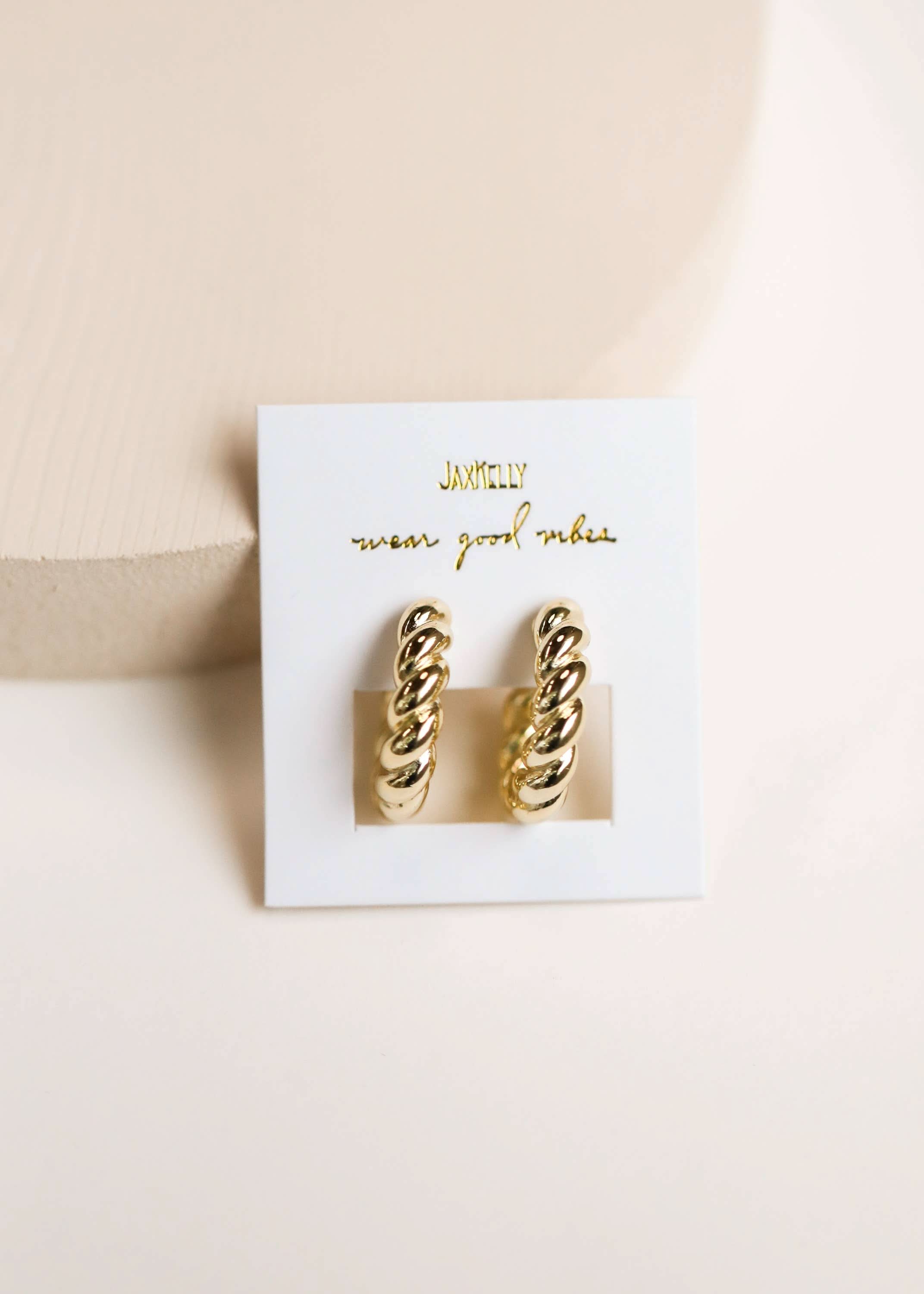 Gold hoop earrings on a white card with gold text against a beige background