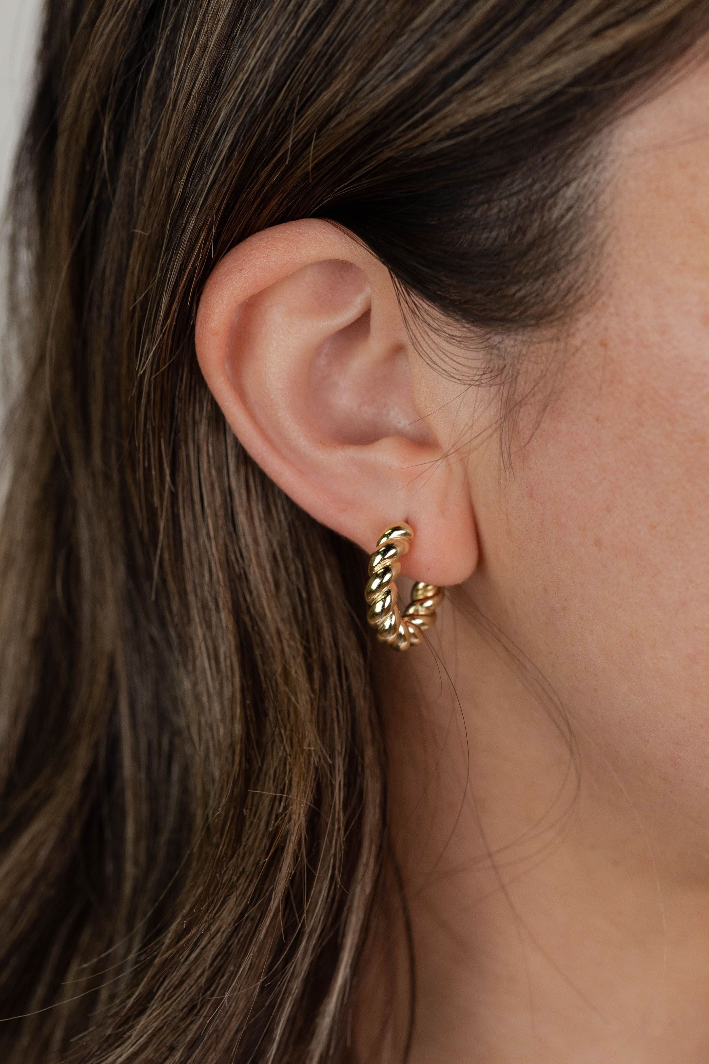 Close-up of a person wearing a gold hoop earring with a neutral background