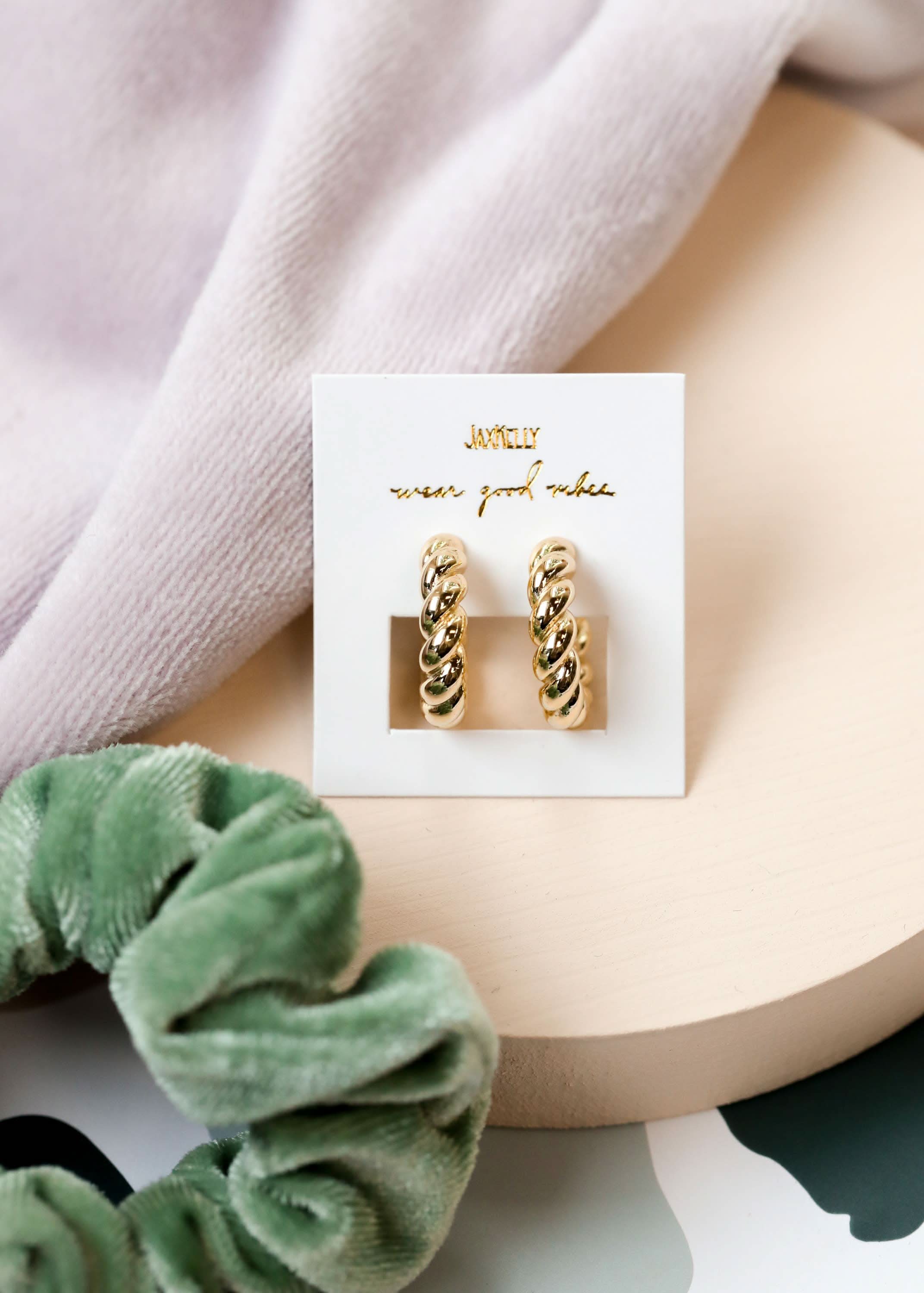 Gold hoop earrings on a branded card with a green scrunchie