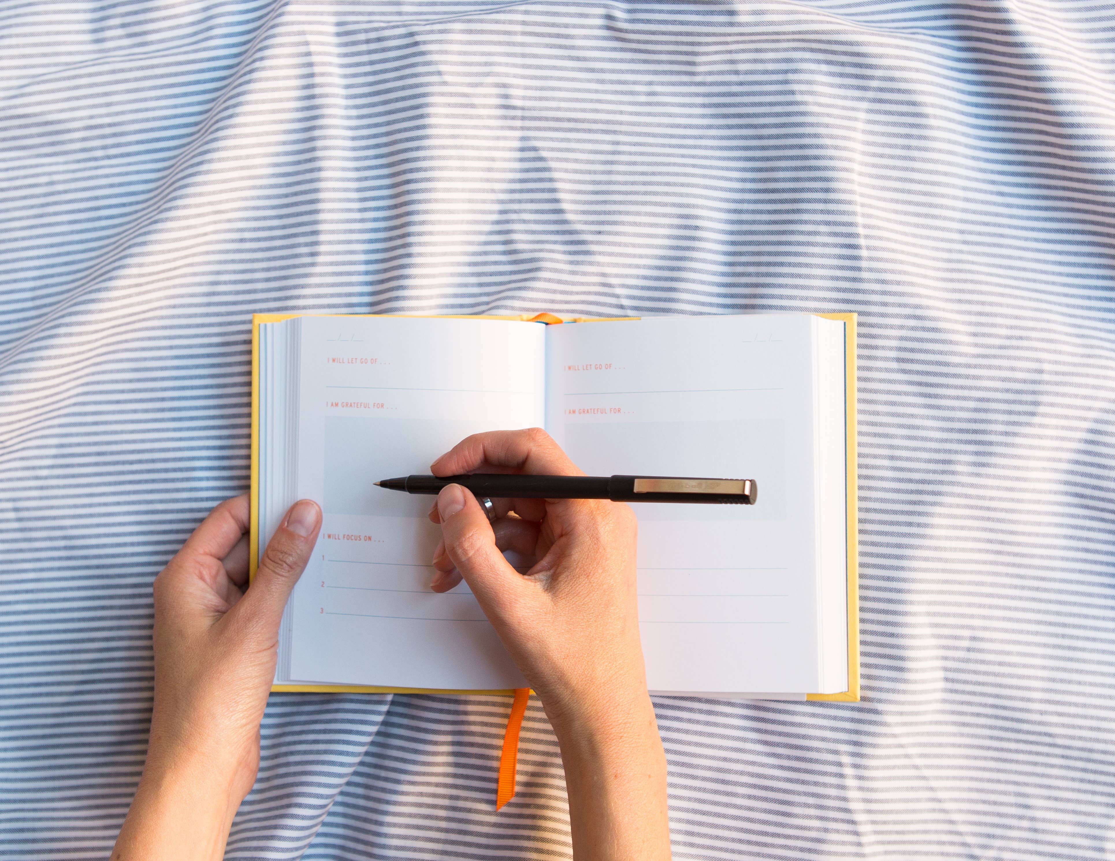 Person writing in a notebook with a pen on a striped fabric background