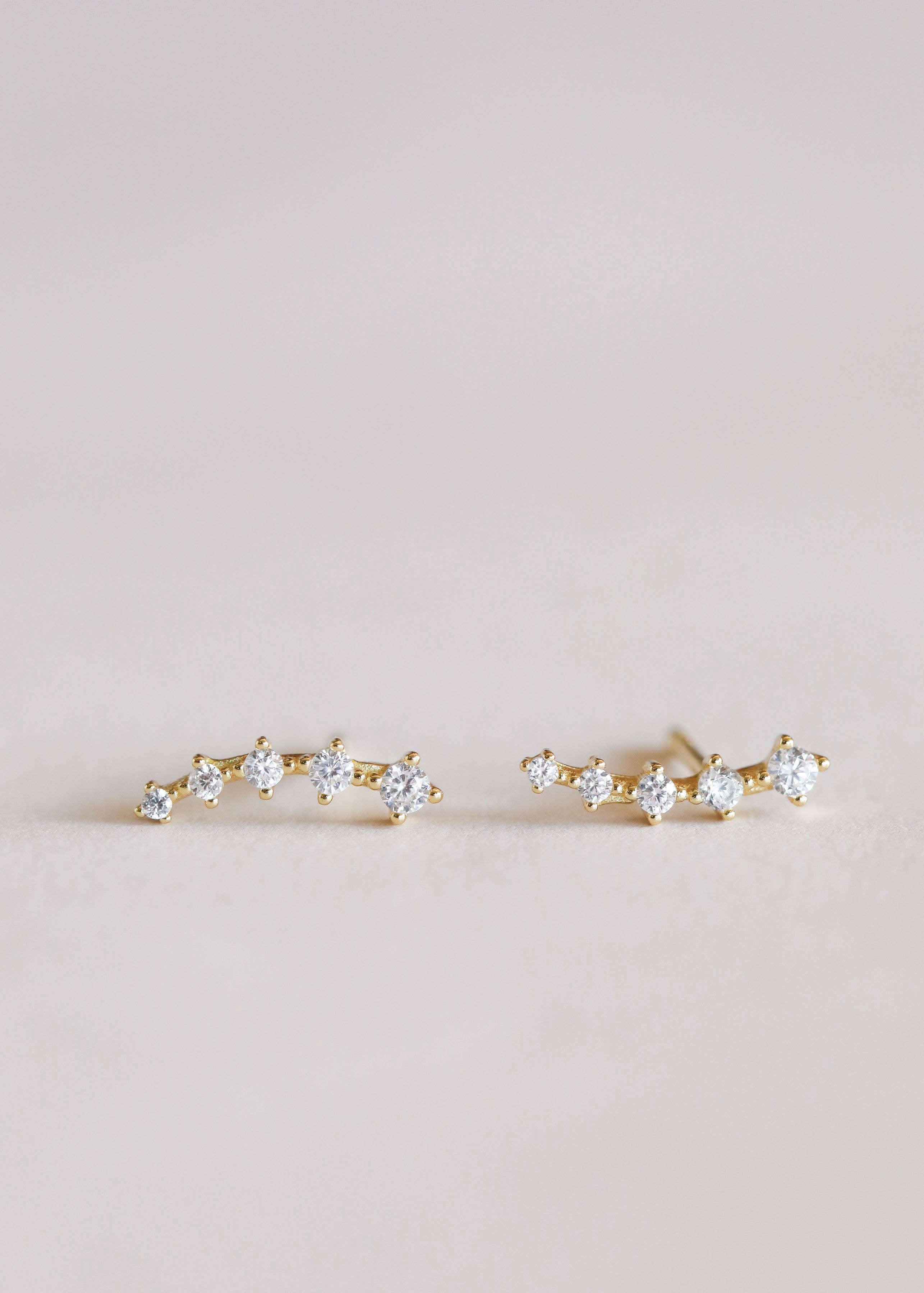 Pair of gold earrings with clear gemstones on a light pink background