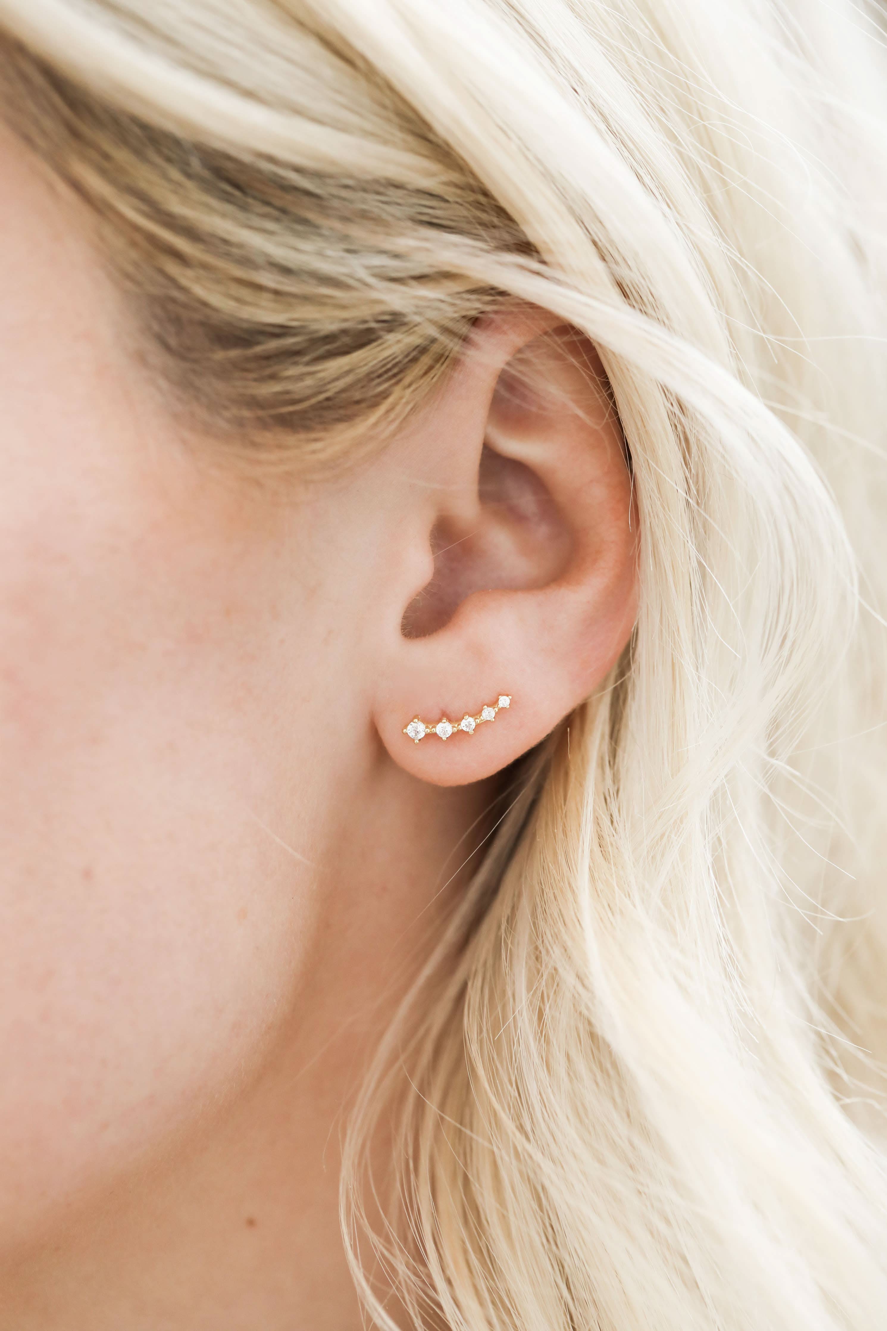 Close-up of an ear wearing a gold stud earring with small diamonds.