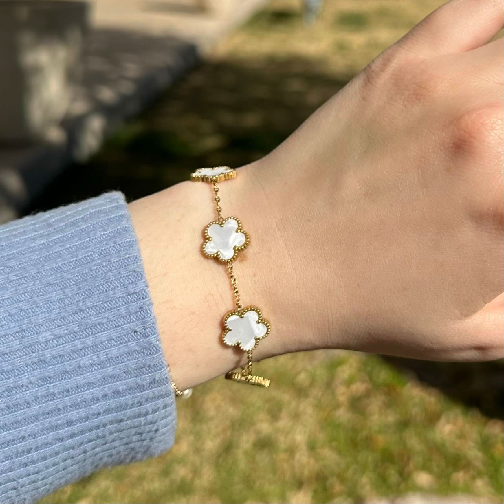 Gold bracelet with white flower charms on a wrist against a blurred 
