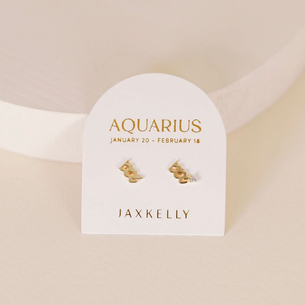 Gold zodiac charm studs in the shape of Aquarius astrological sign displayed on earring card
