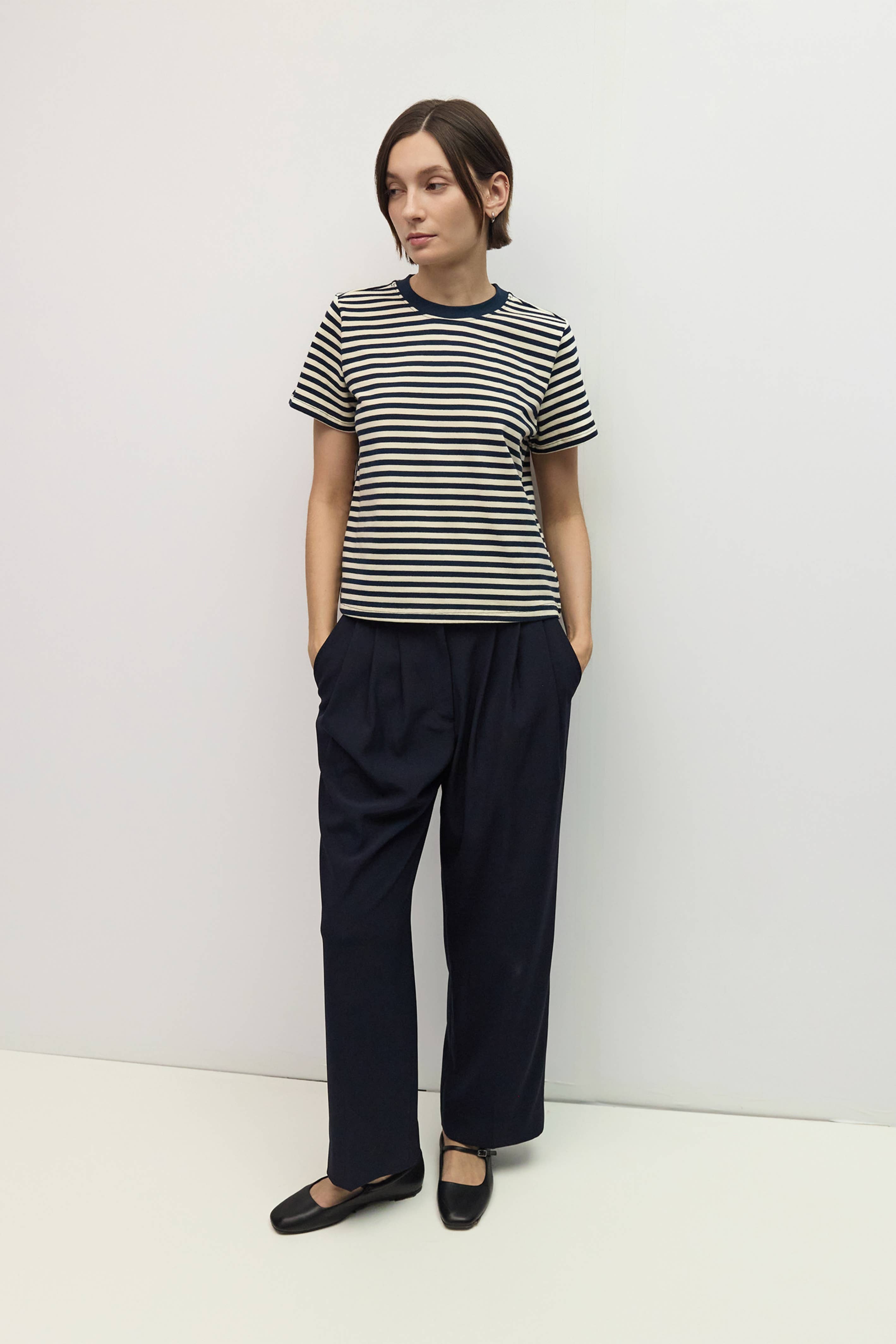 Person wearing a striped shirt and dark pants against a white background