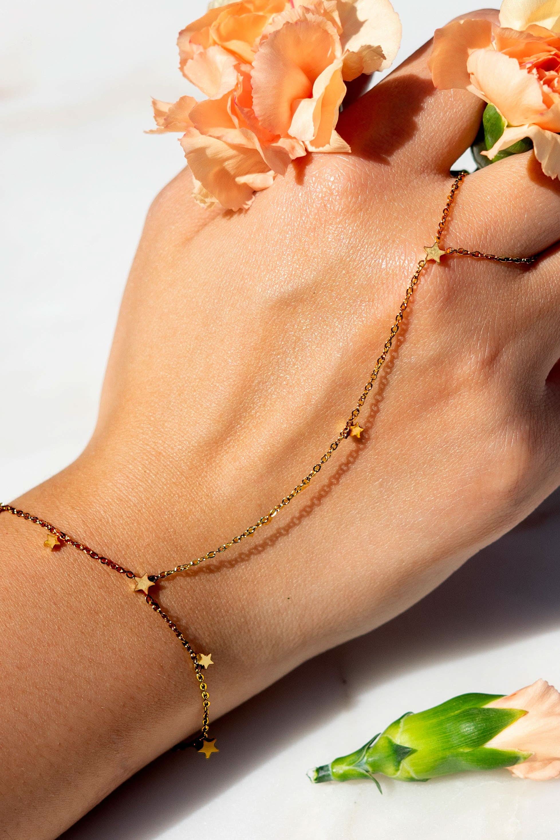 Hand wearing a delicate gold hand chain bracelet connected to a thin ring