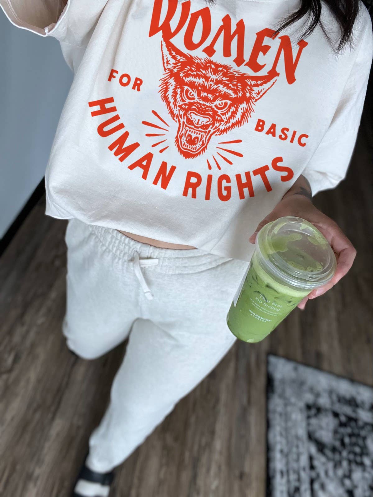 Person wearing a white hoodie with red text and graphic, holding a green cup.