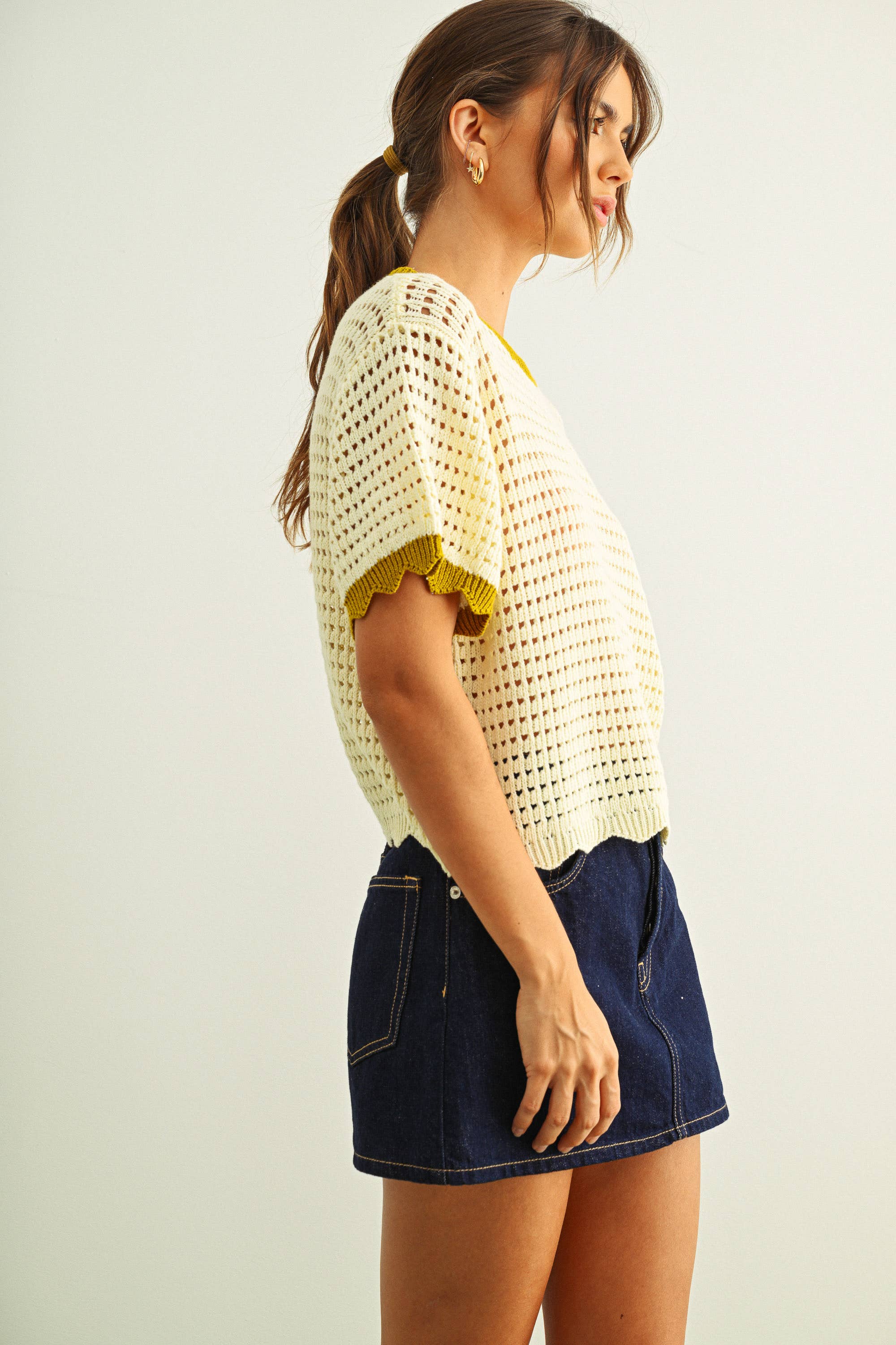 Woman wearing a white crochet top and denim skirt on a plain background