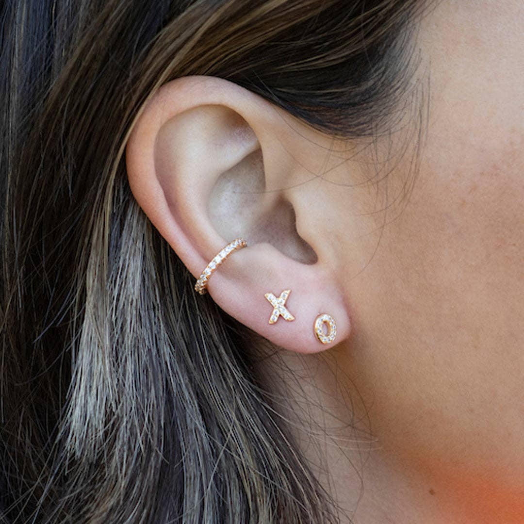 Close-up of an ear wearing gold earrings with 'XO' design.