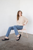 Woman wearing flip flops, blue jeans, and a natural beige button up piper cardigan 