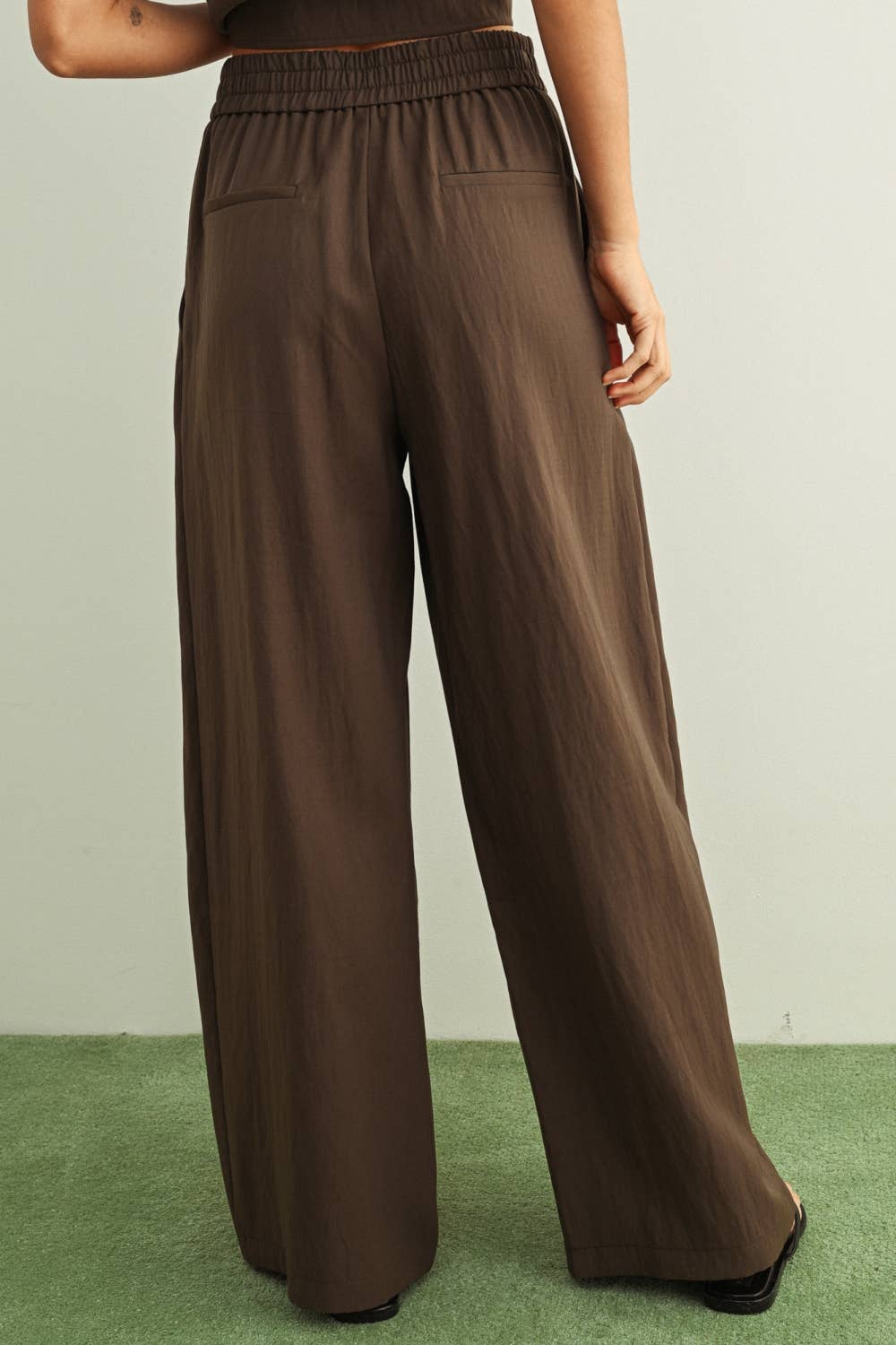 Brown wide-leg pants worn by a person on a green floor with a light gray wall background