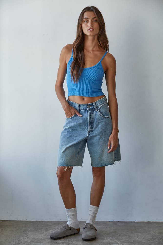 Woman wearing a blue tank top and denim shorts against a plain background
