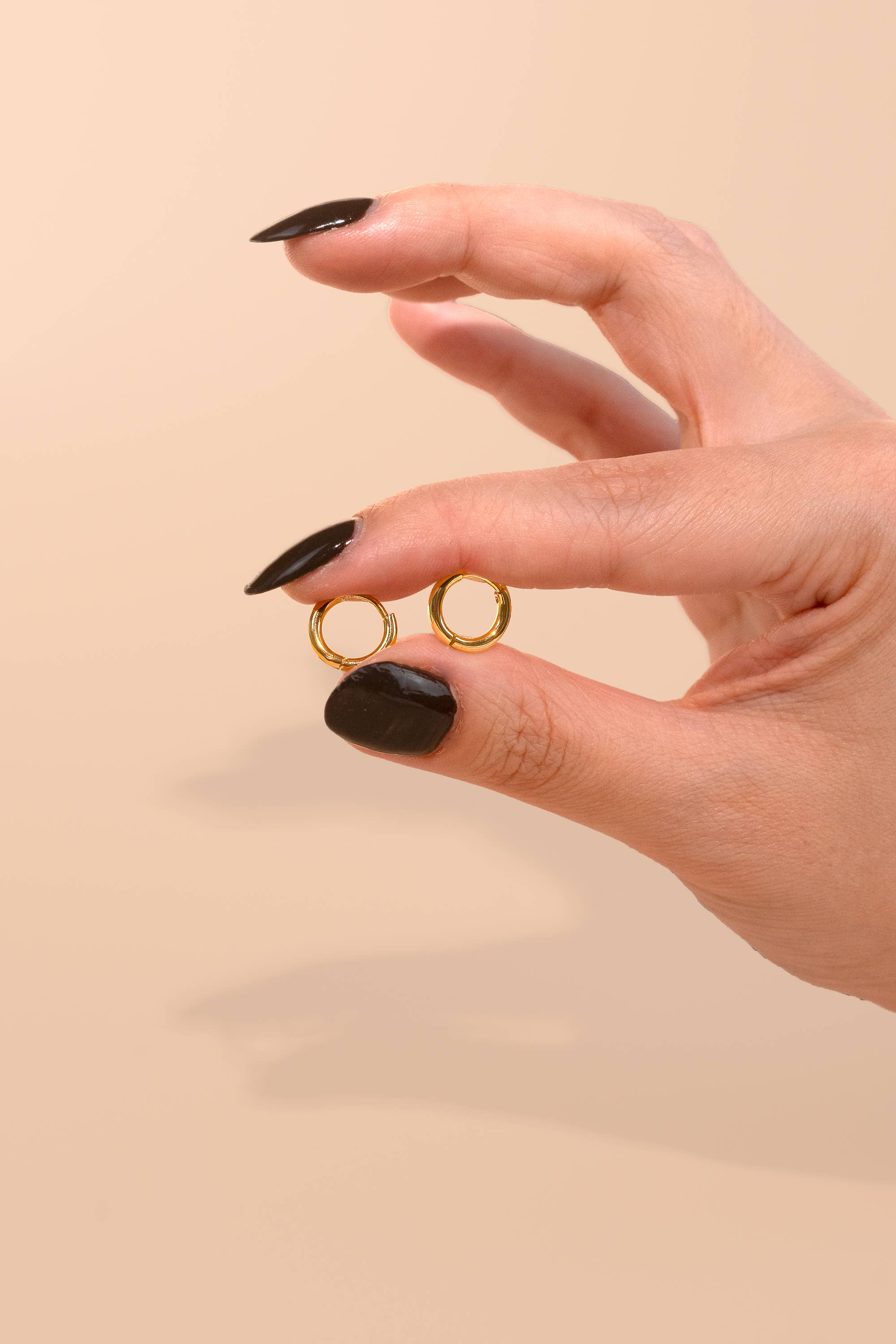 Woman holding the everyday gold Huggies medium sized hoops on a pink peach background 
