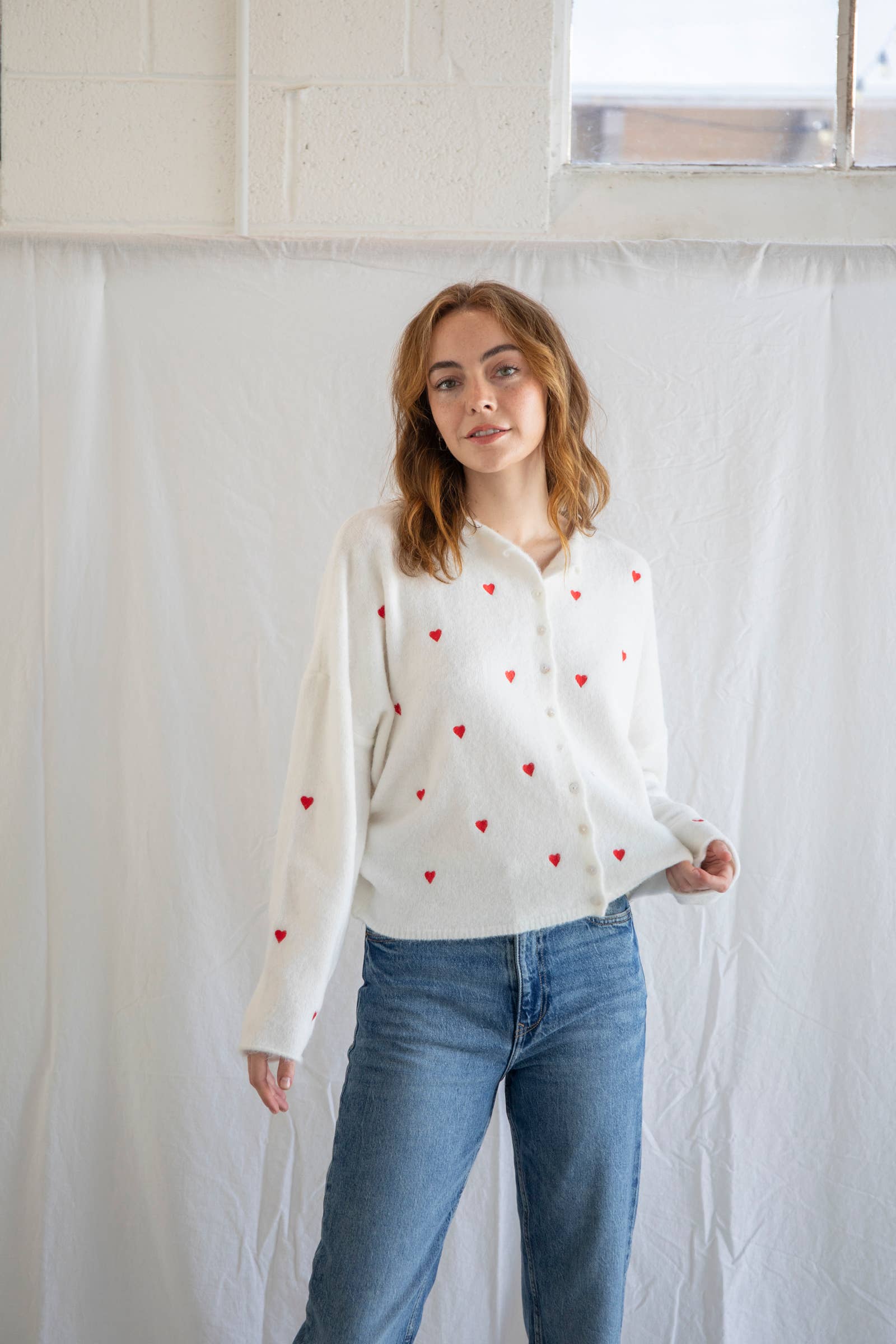 Woman wearing a cream cardigan with red hearts and buttons and blue jeans
