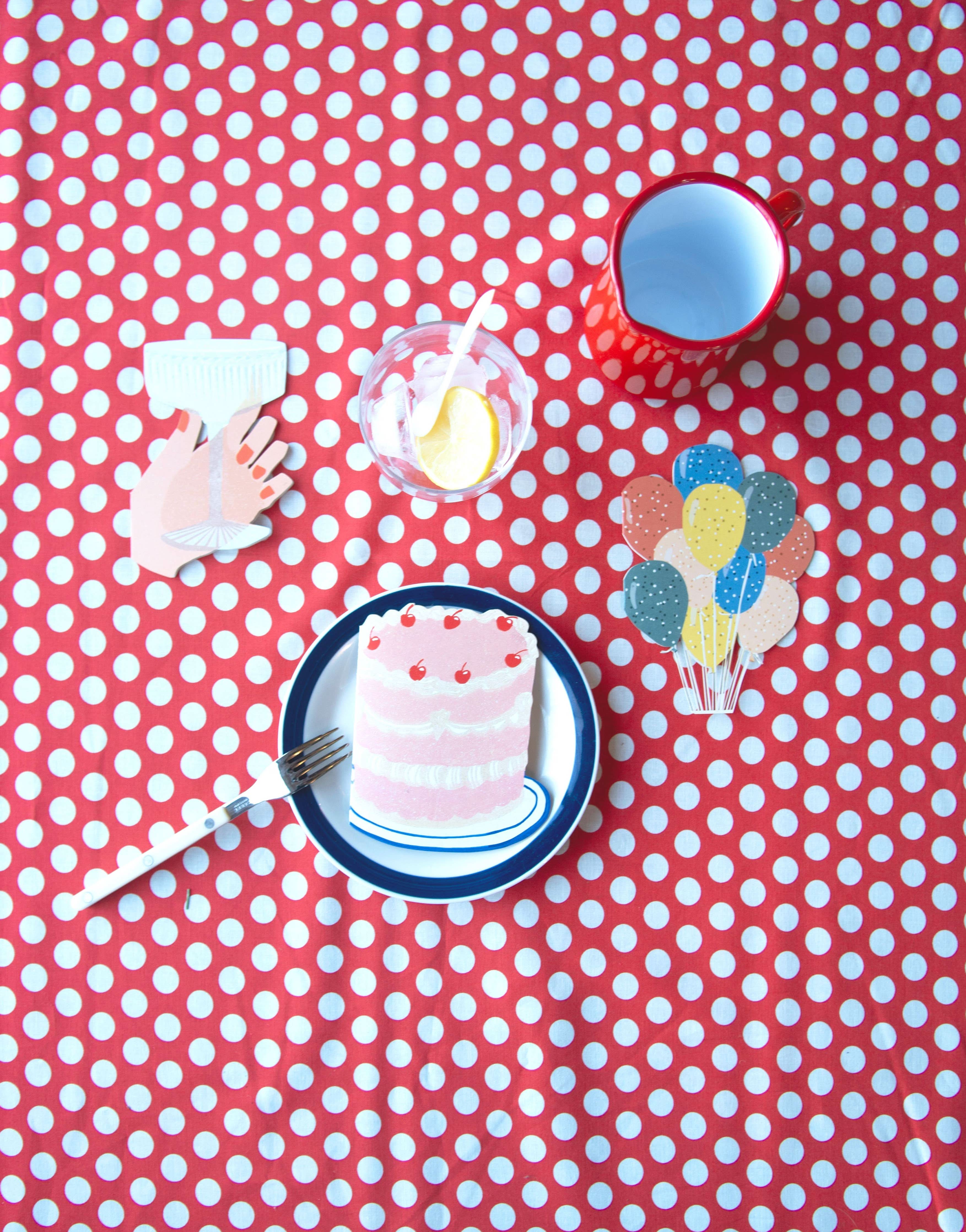 Three layer cake with cherries on top card with a hand holding a glass card, a colorful balloons card, a red mug, and clear cup with lemons inside on a red and white polka dot background. 