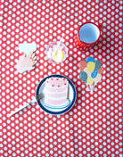 Three layer cake with cherries on top card with a hand holding a glass card, a colorful balloons card, a red mug, and clear cup with lemons inside on a red and white polka dot background. 