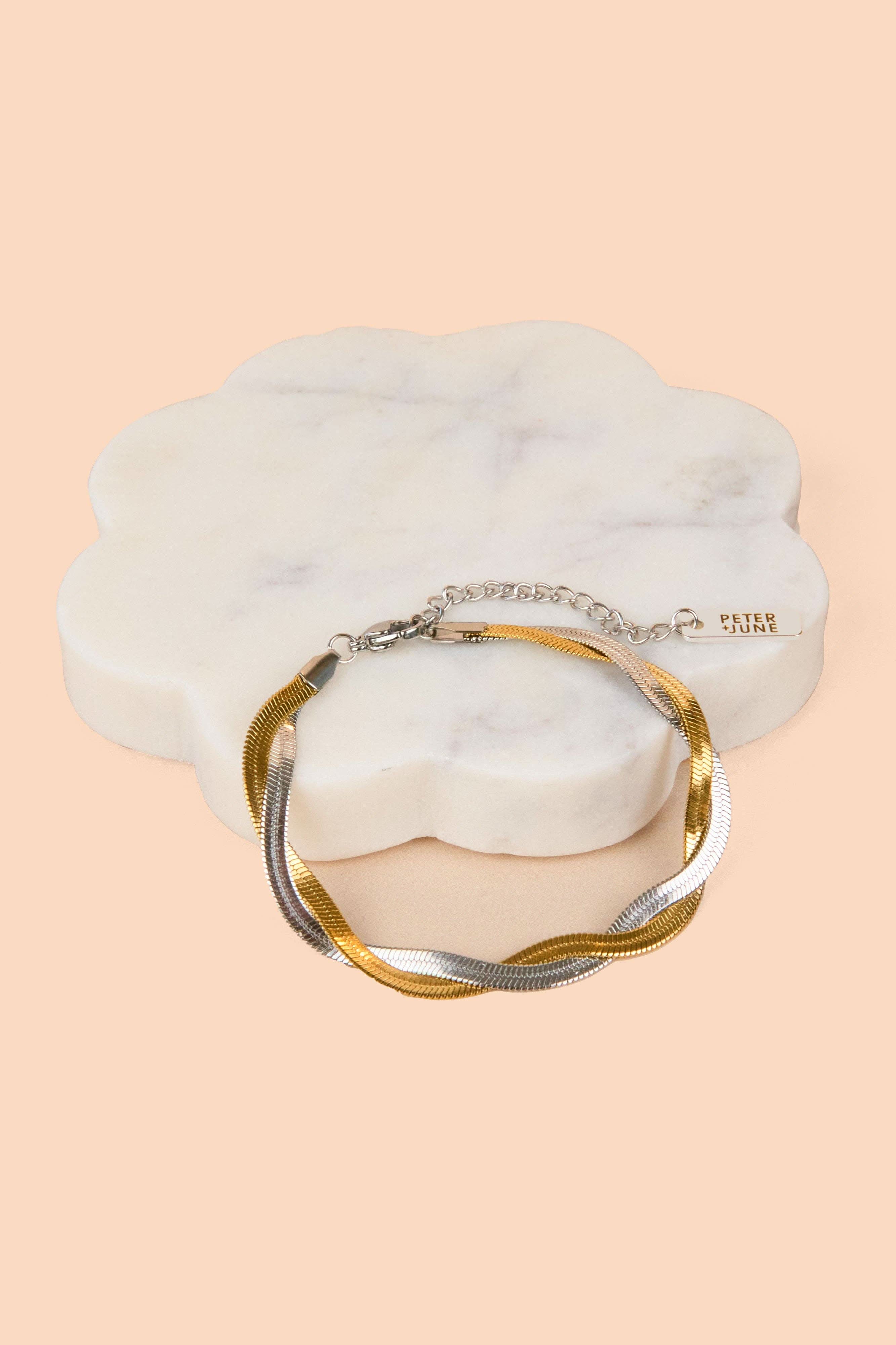 Gold and silver bracelet on a marble surface with a beige background