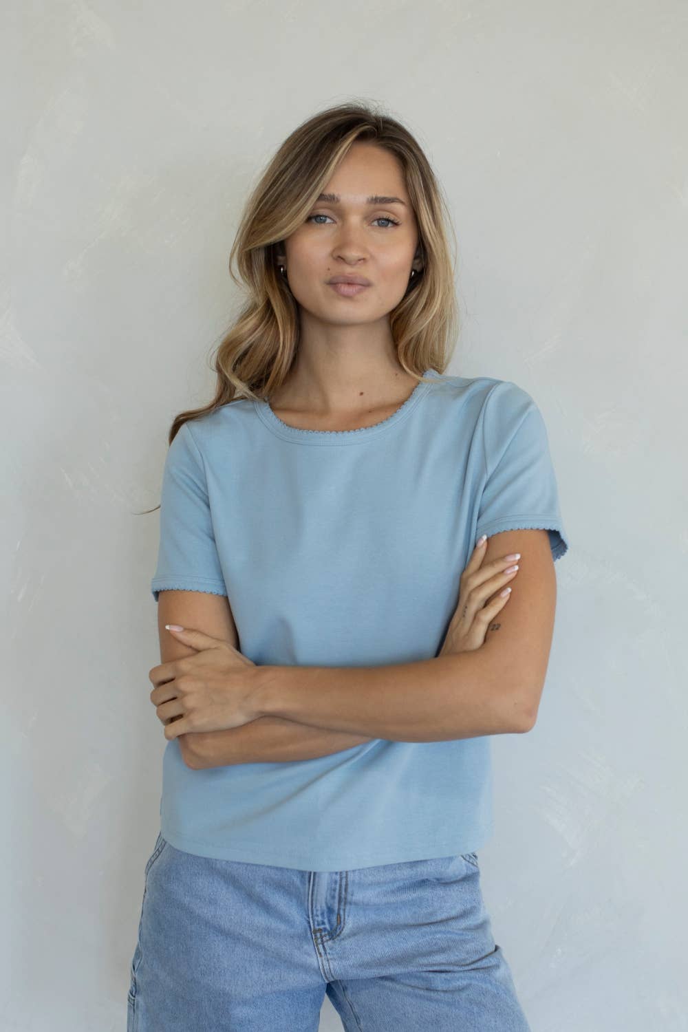 Woman wearing a light blue t-shirt and jeans against a plain background
