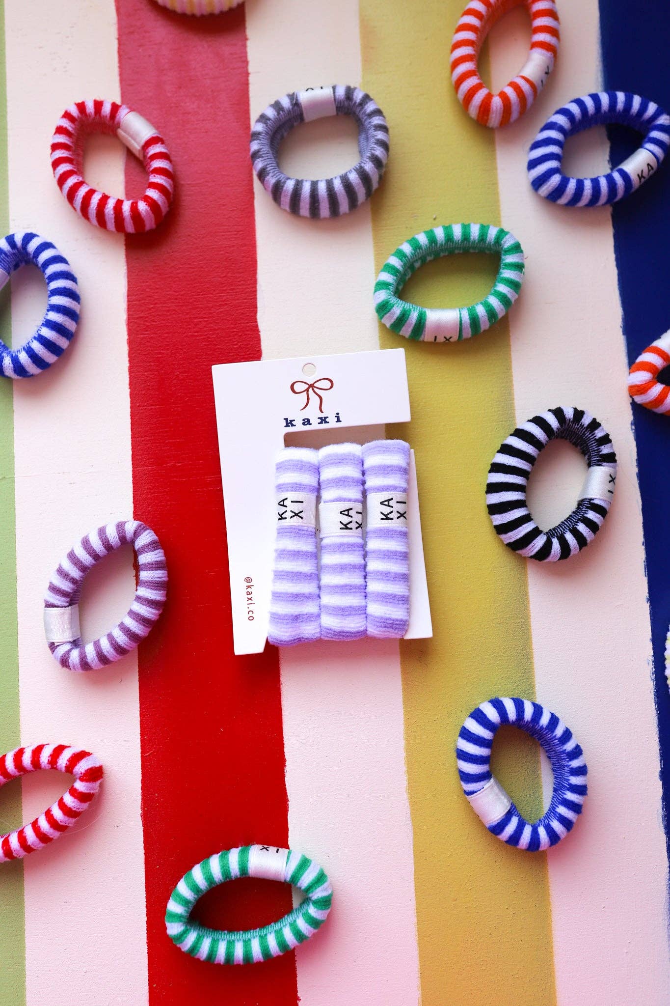 Colorful hair ties on a multicolored striped background with Kazi packaging.
