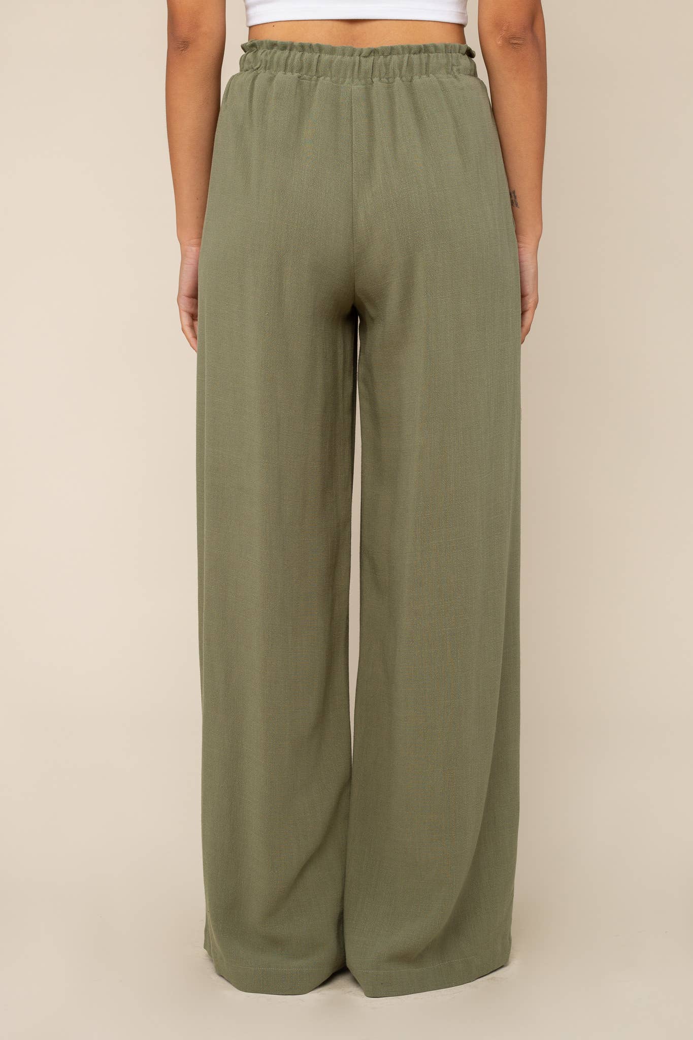Woman facing away from the camera wearing Sage green, wide leg, cove linen pant and white tee