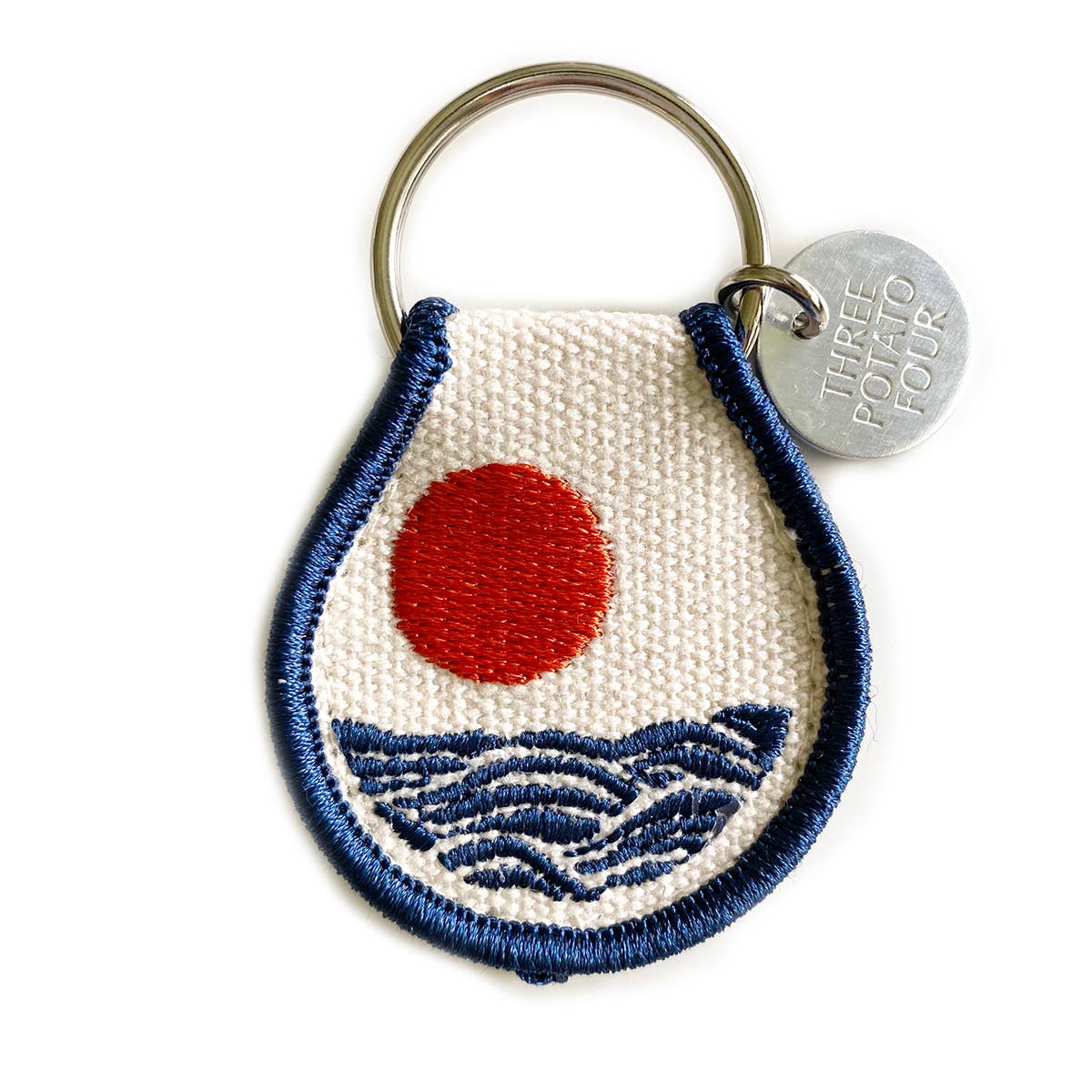 Keychain with embroidered design of a red circle and blue waves on a white background