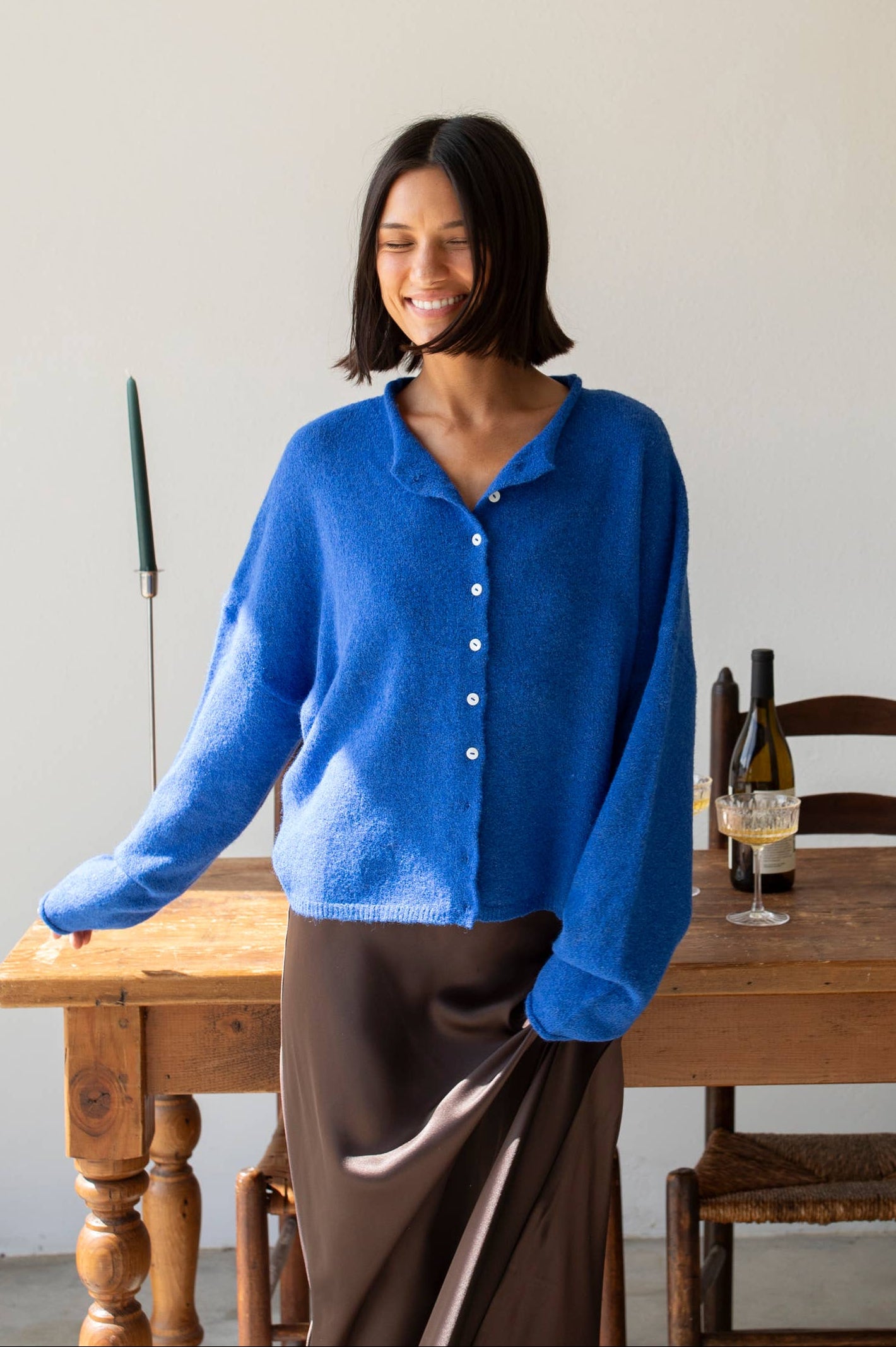 Woman wearing a blue cardigan standing in a room with wooden furniture.