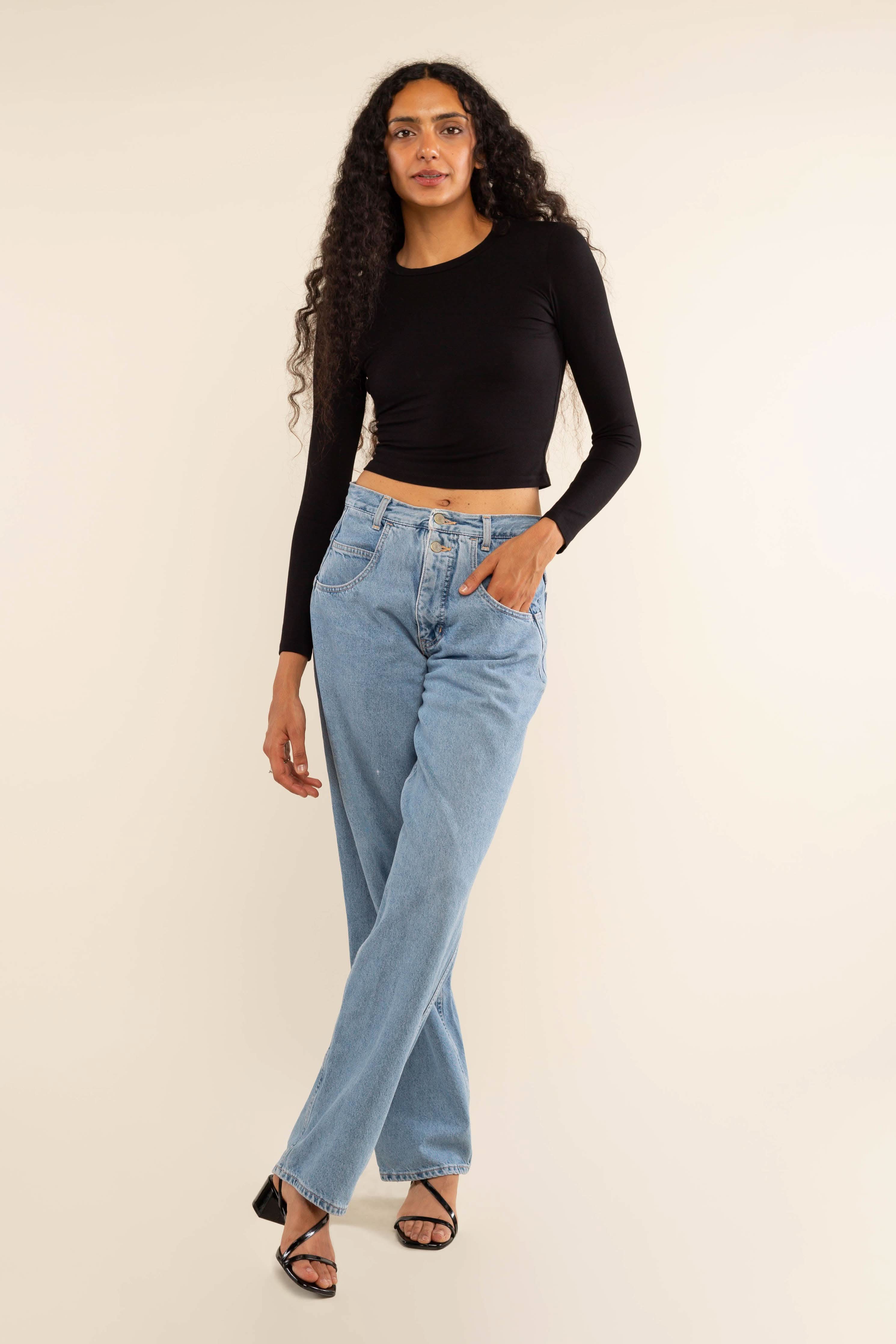Woman wearing white, long sleeve, tight, crew neck, top with blue jeans