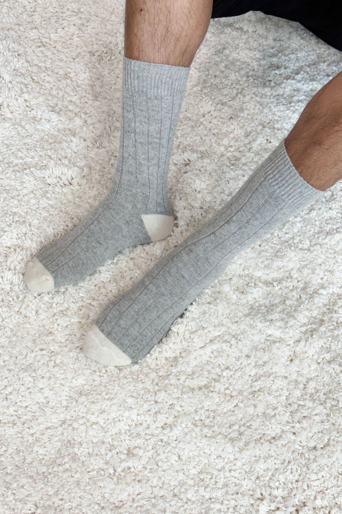 Man wearing grey socks that go up to the calf with crème coloring on the heel and toe. 