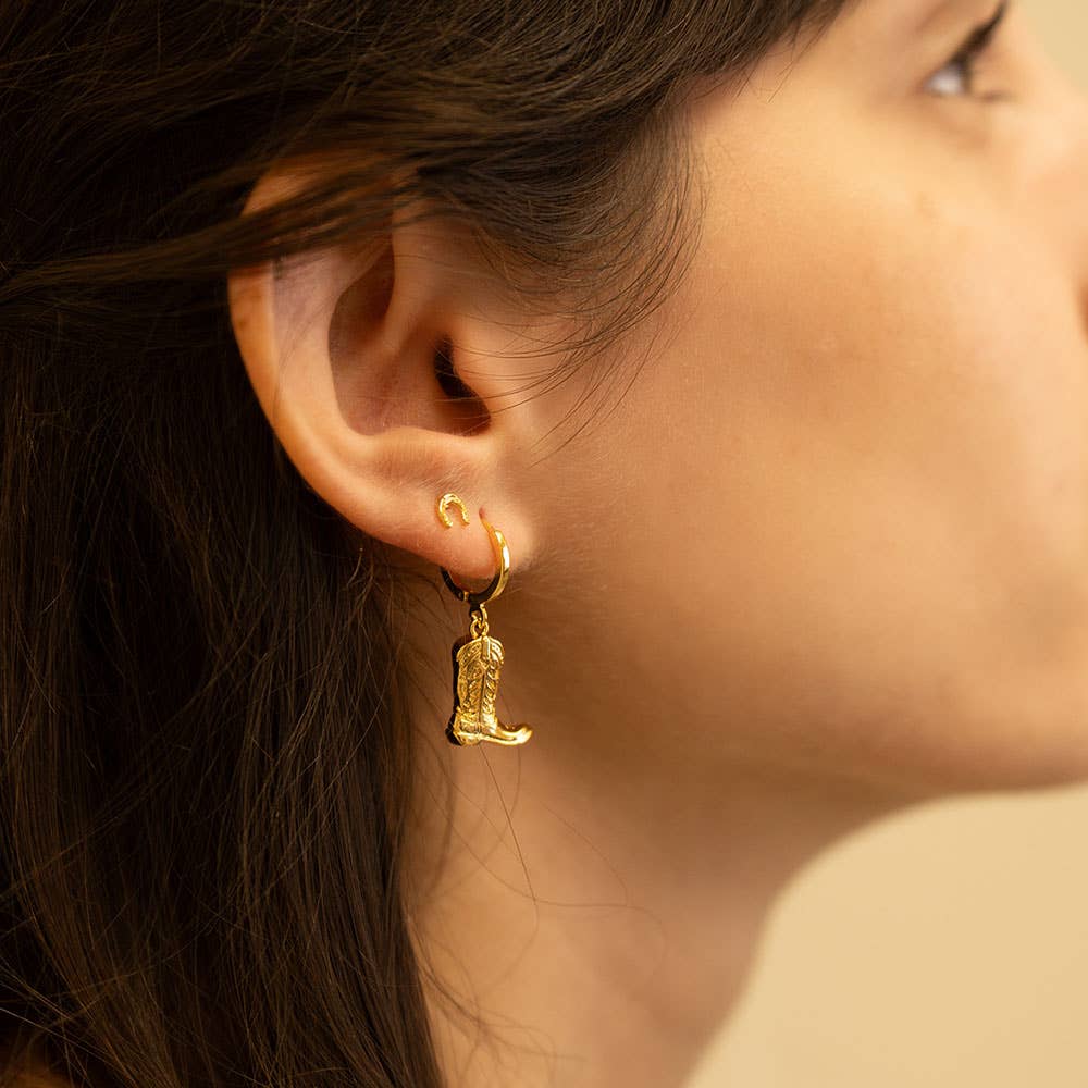 Close-up of a person wearing a gold earring with a boot design.