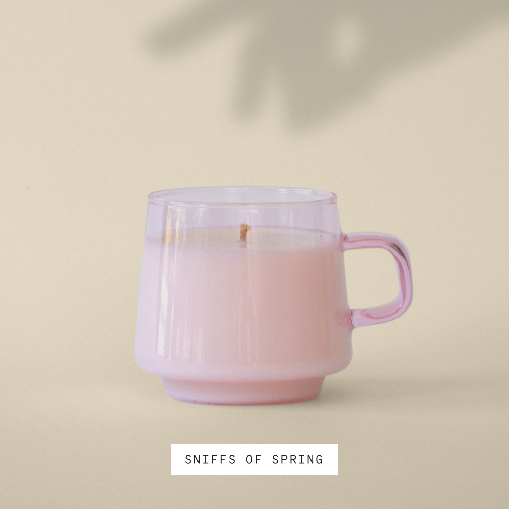 Candle in pink opaque reusable, stackable mug sitting in the sun against a cream colored wall