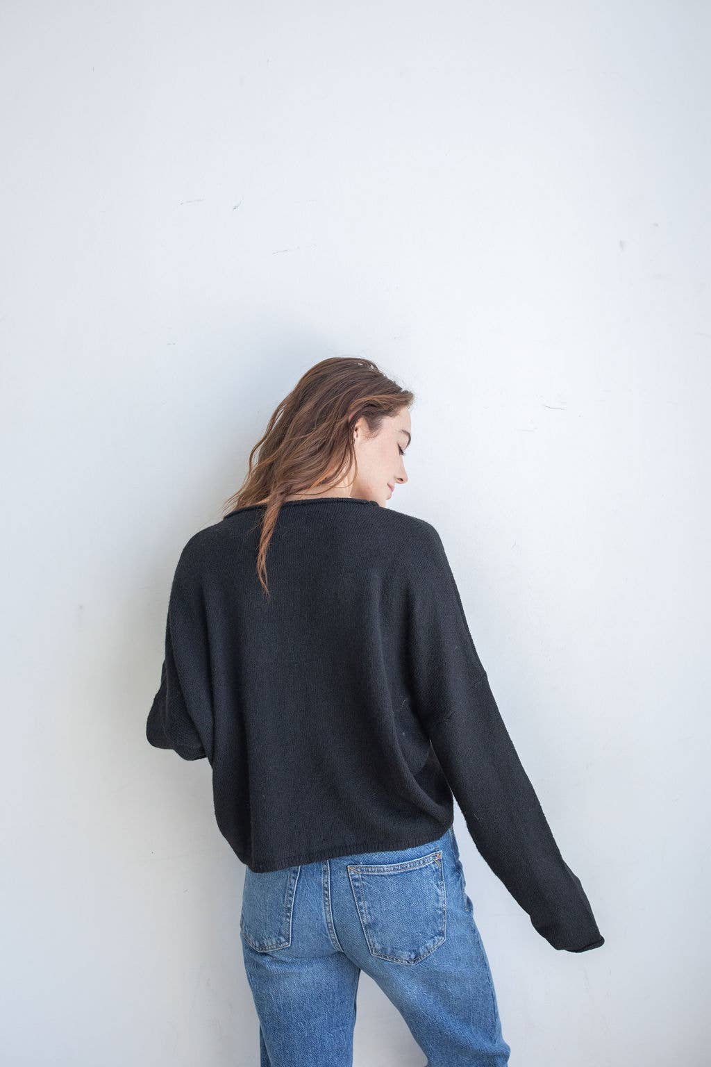 Woman wearing black cardigan facing backward and blue jeans 