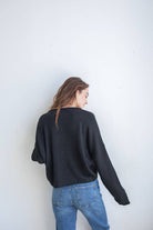 Woman wearing black cardigan facing backward and blue jeans 