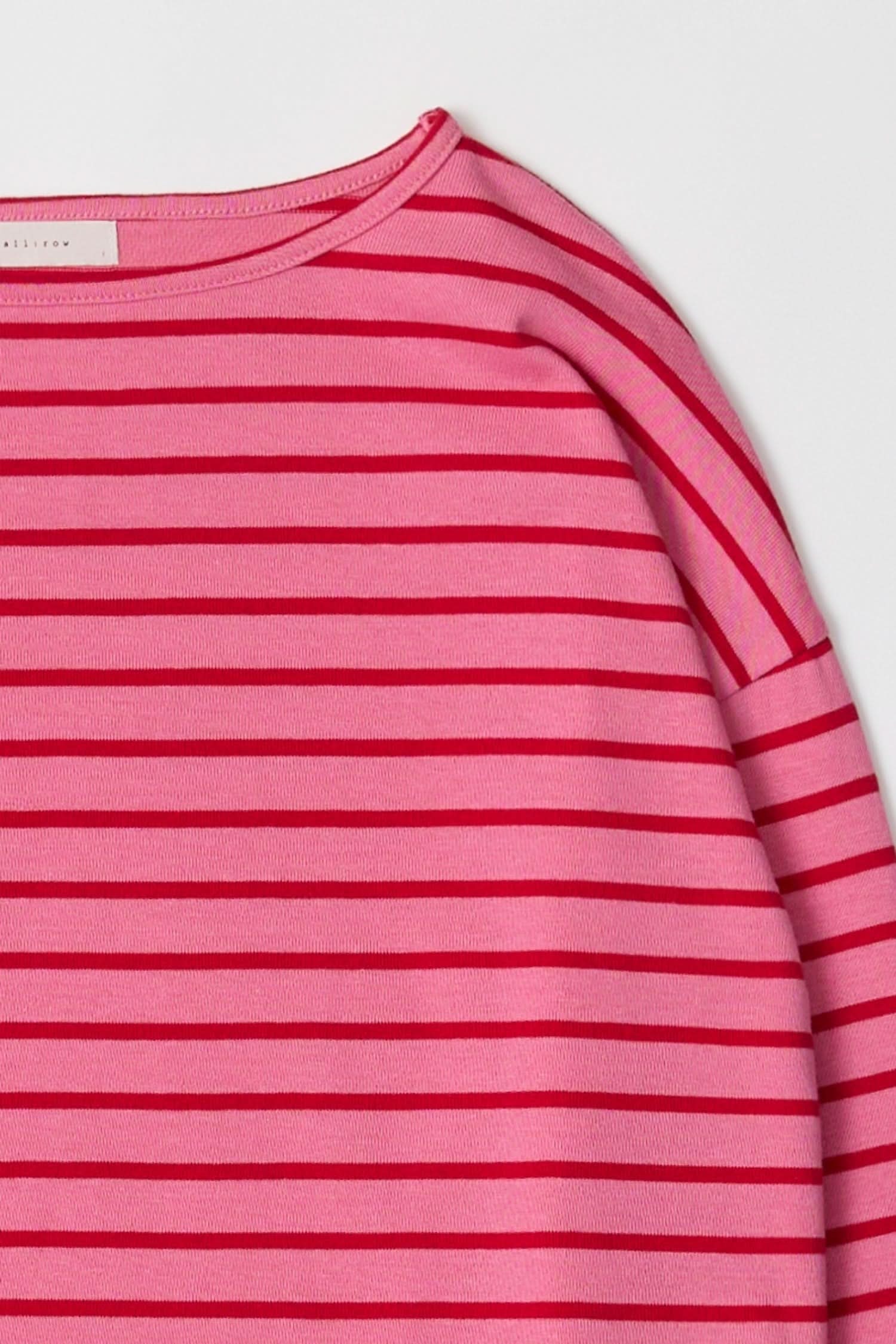 Close up of long sleeve, pink, pullover sweater with thin red horizontal stripes