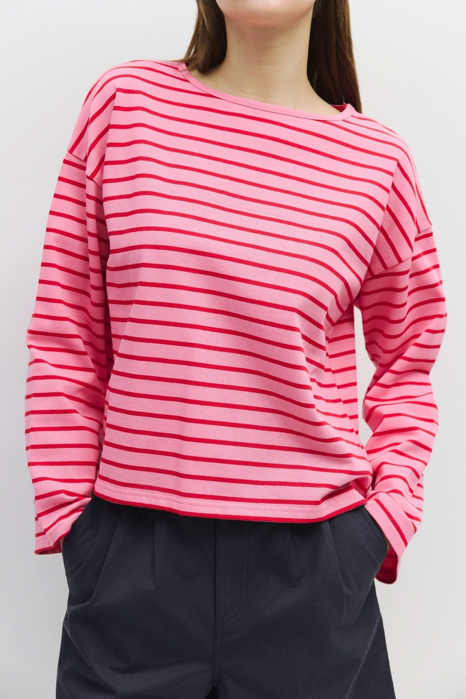 Woman wearing long sleeve, pink, pullover sweater with thin red horizontal stripes 