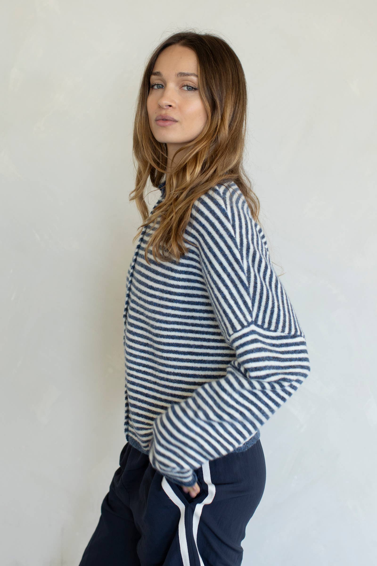 Woman wearing a striped sweater and dark pants against a plain background