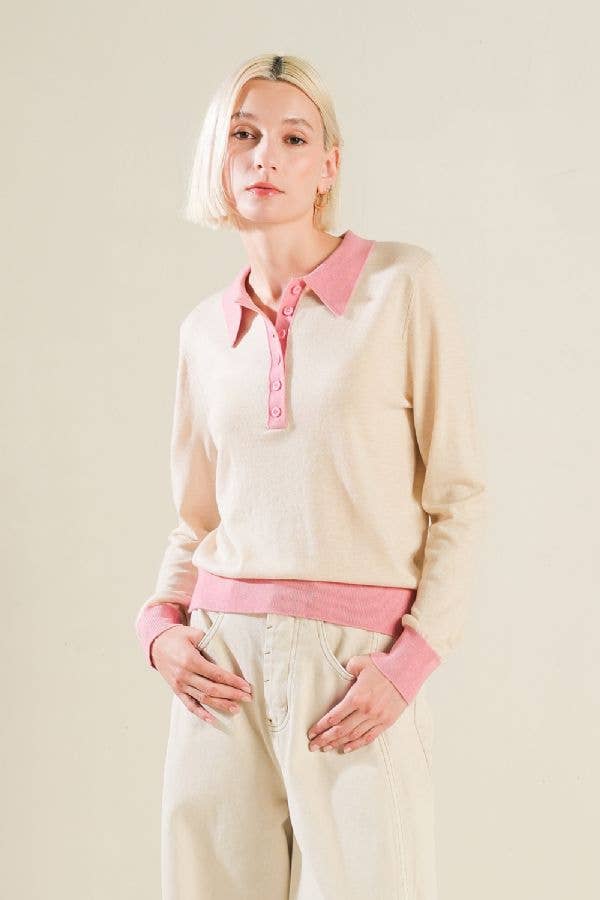 Person wearing a cream sweater with pink collar and cuffs on a plain background