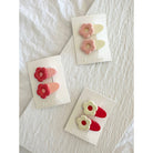 Three sets of mini flower clips in red, pink and white clipped to display card stock laying on white cloth