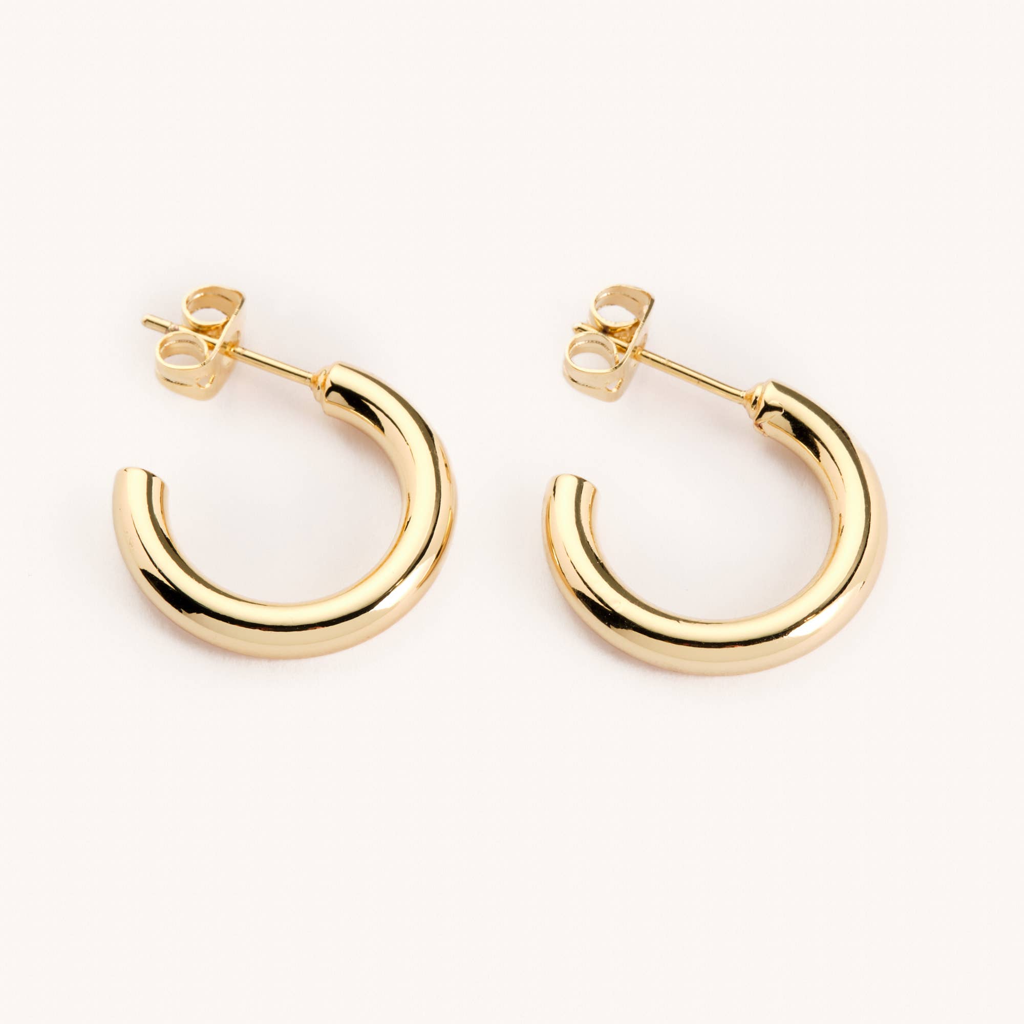 gold medium sized tube hoop earrings laying on a white background 