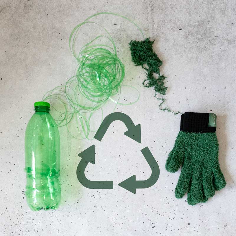 Recycling theme with green bottle, gloves, and yarn on a concrete surface.