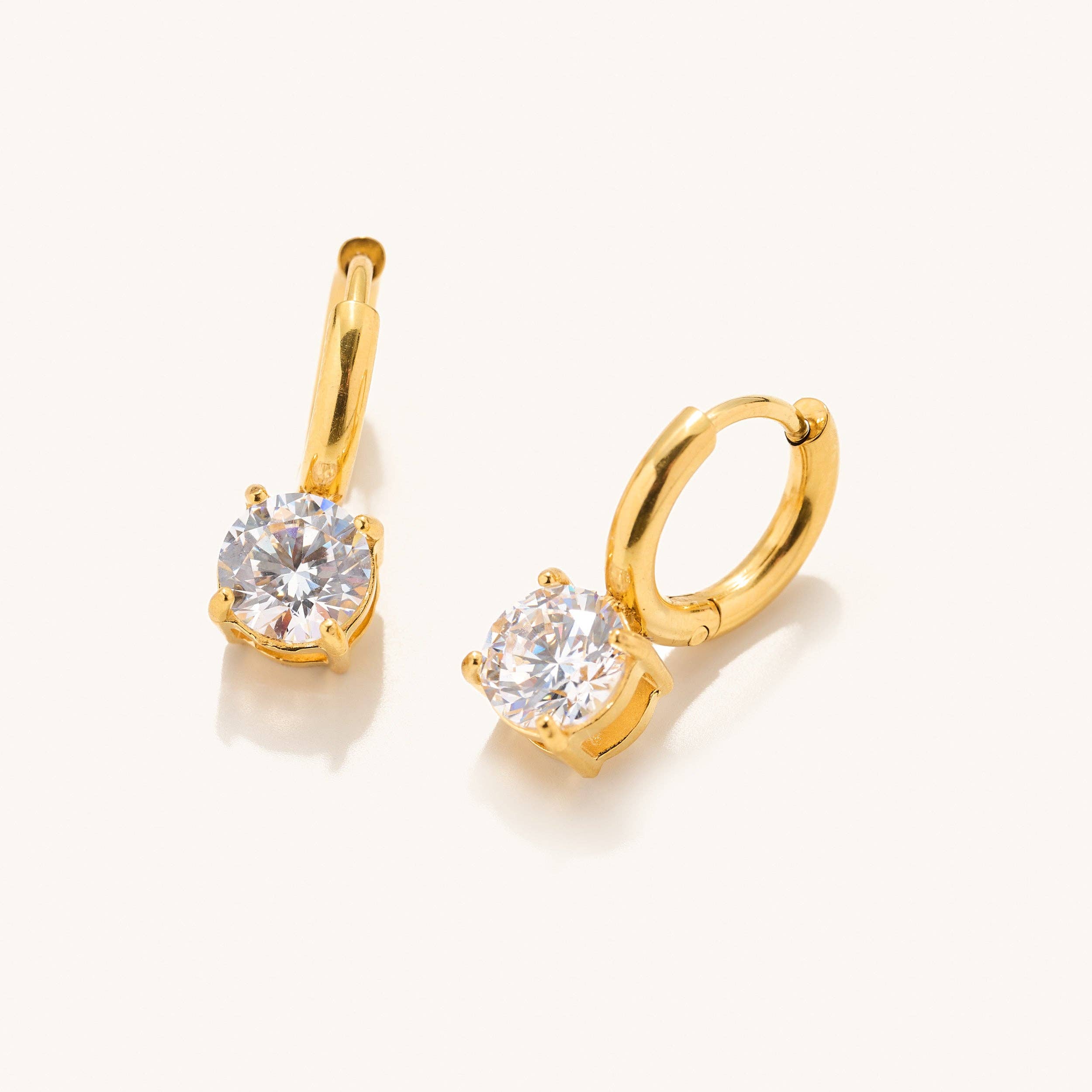 Gold huggie earrings with gem dangle detail laying on a white backdrop