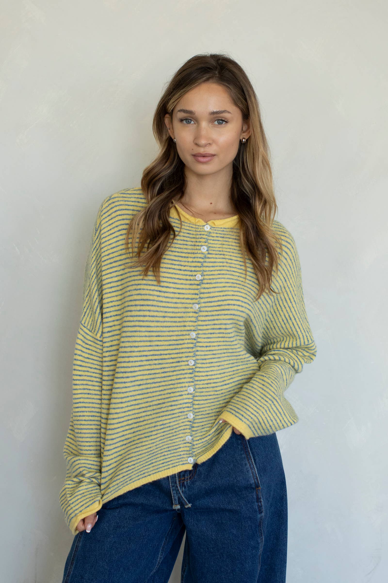 Woman wearing a yellow striped shirt and blue jeans against a plain background
