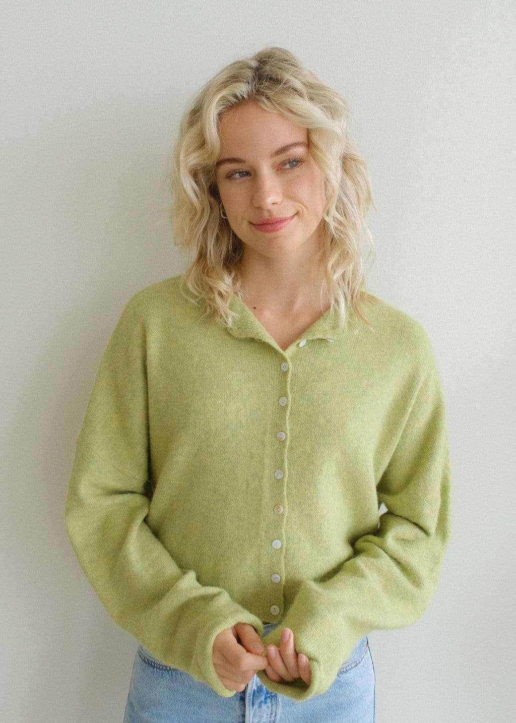 Woman with blonde hair wearing long sleeve lemongrass colored cardigan buttoned up with white buttons 