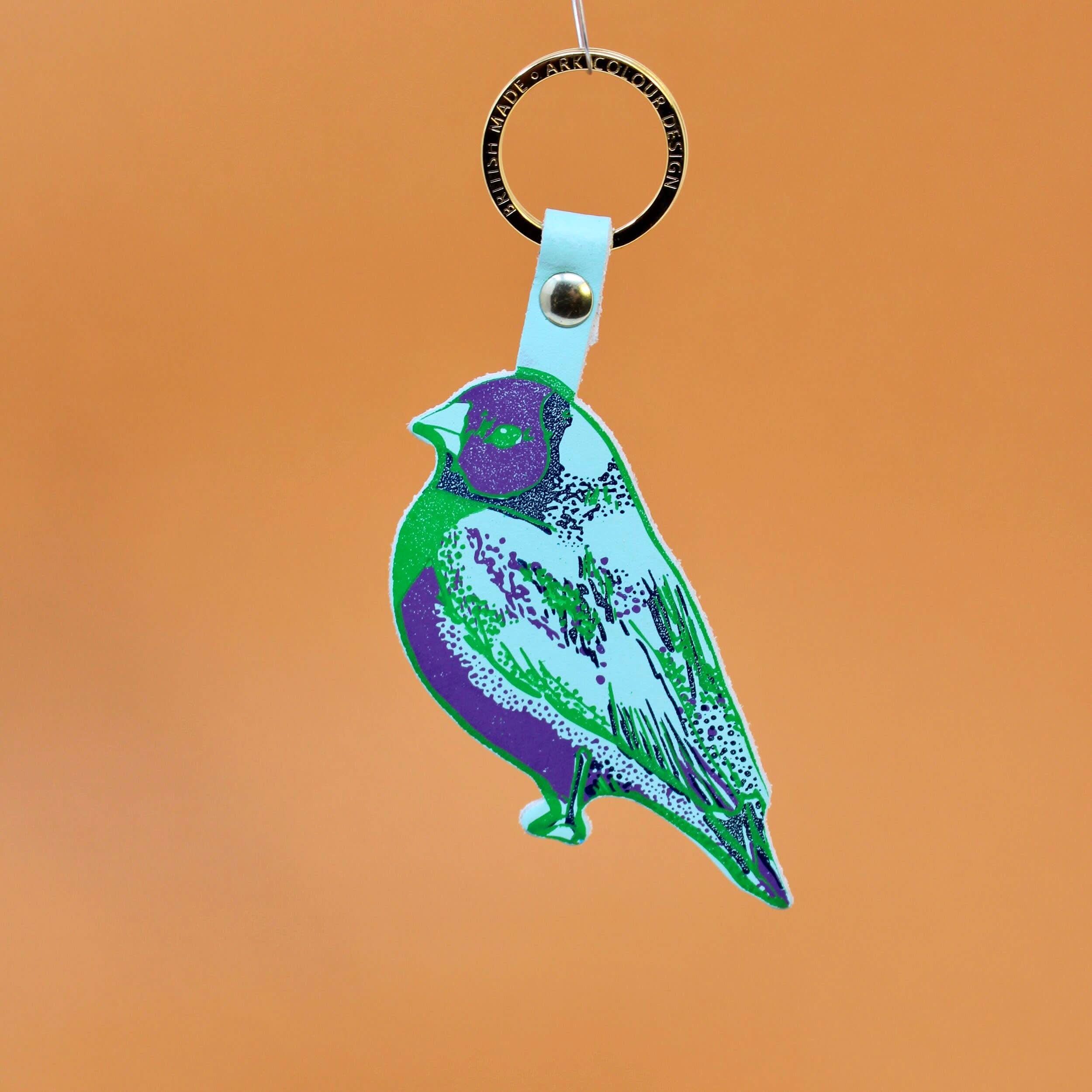 Colorful finch bird keychain behind an orange background. 